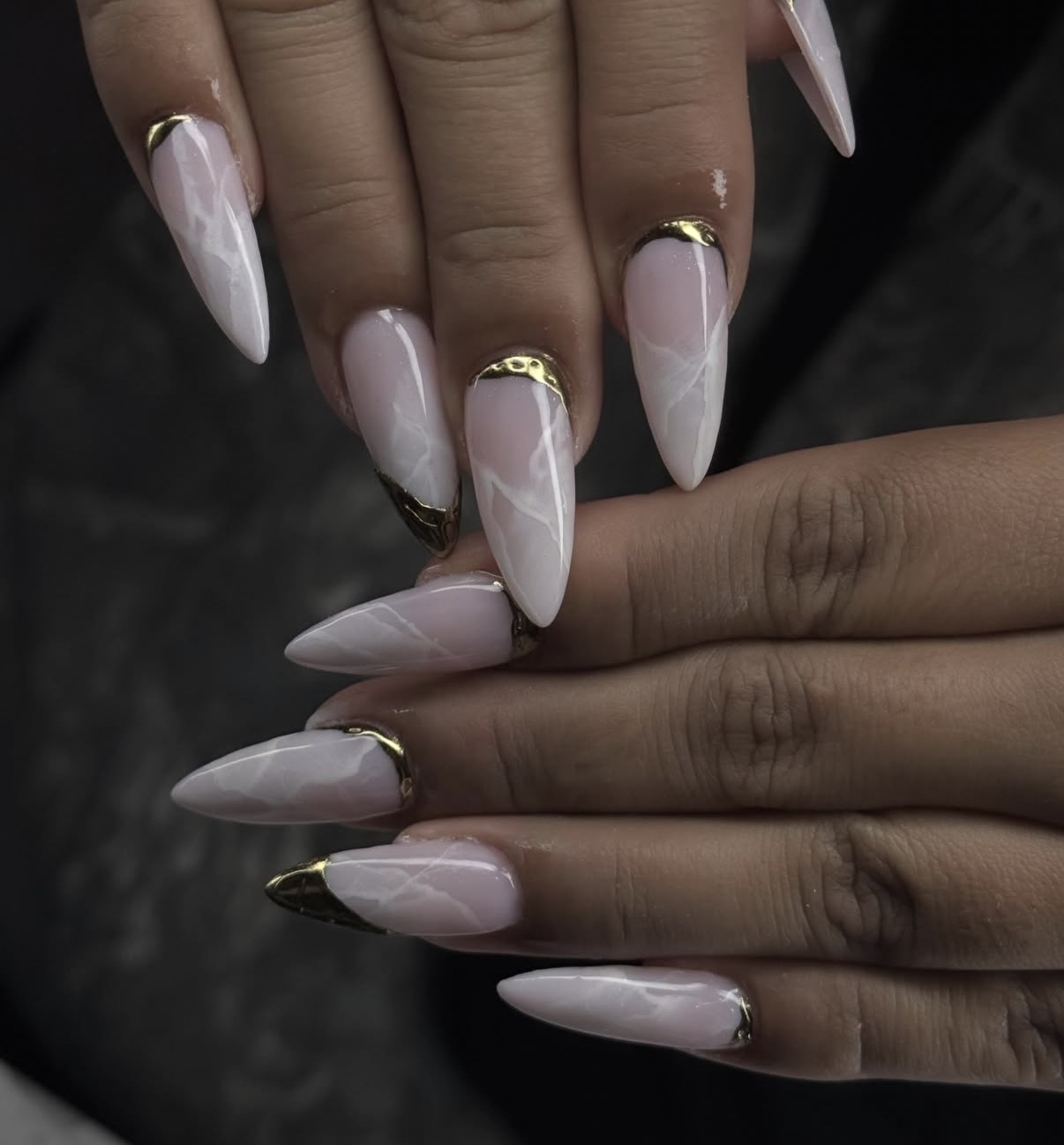 Close-up of hands with long, almond-shaped nails painted in a light pink color with gold accents at the tips.