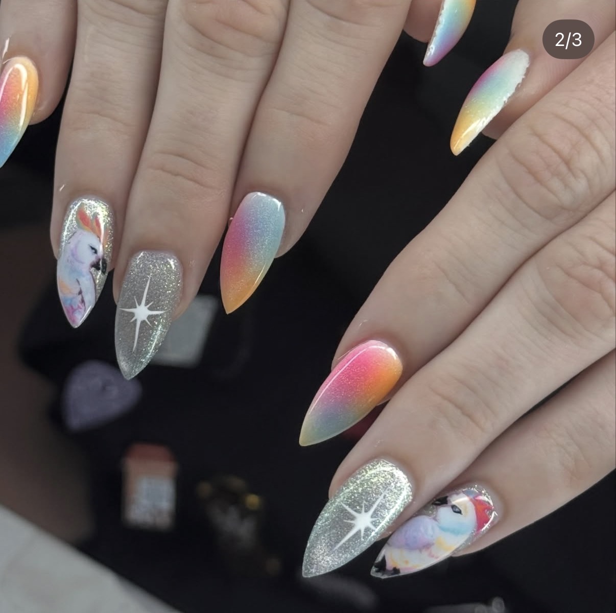 Close-up of hands with colorful, glittery, and holographic nail art featuring unicorns and star designs.