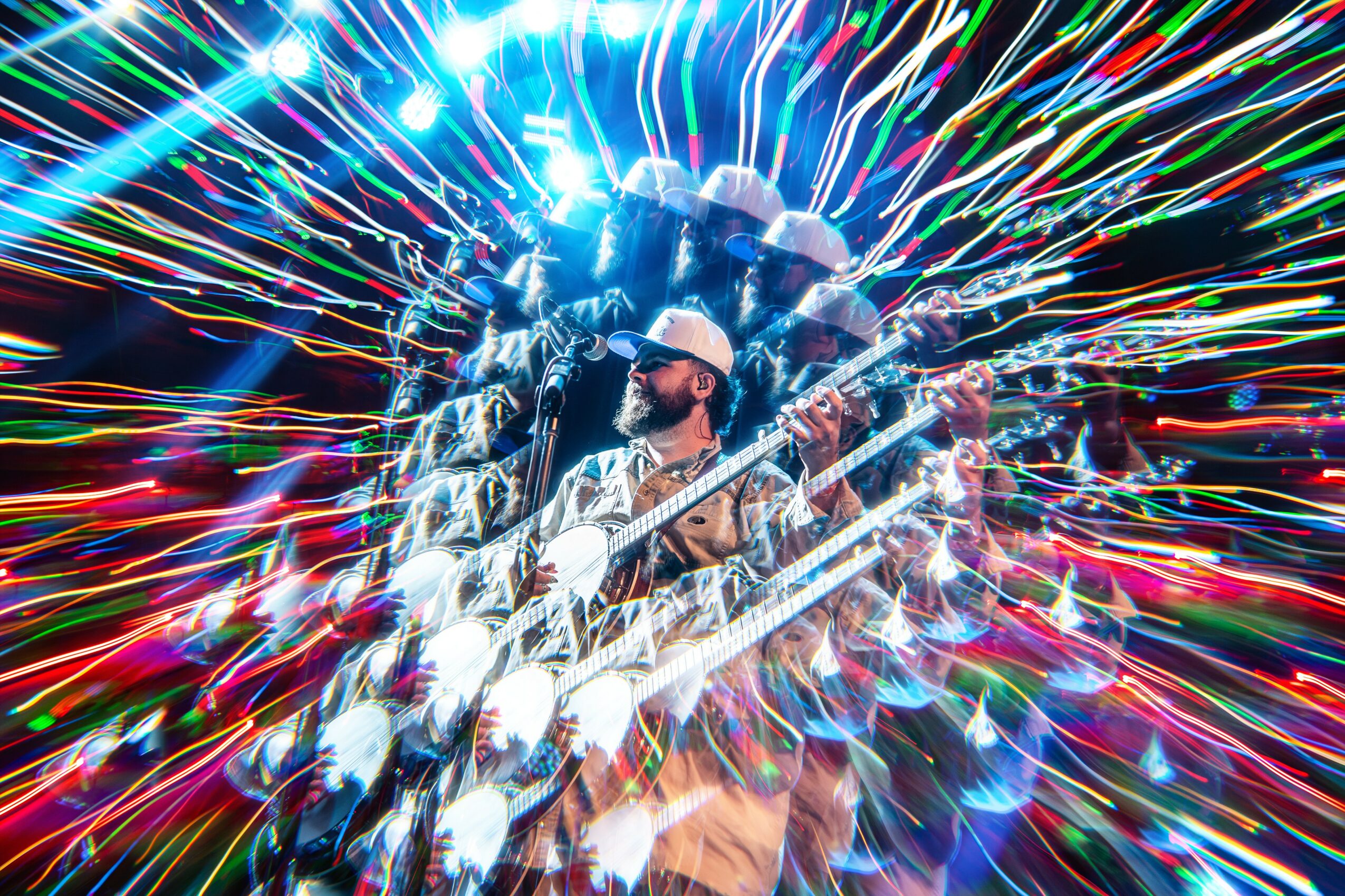 Person wearing a hat and sunglasses playing guitar with colorful light streaks in background
