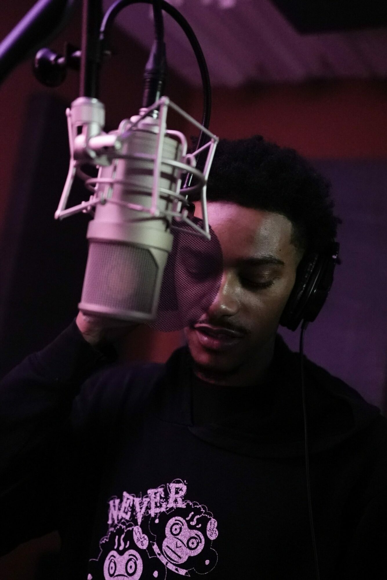 Person singing into a microphone in a recording studio with purple lighting.