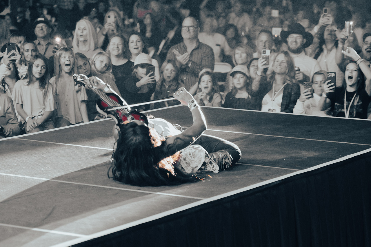 Performer lying on stage with a sword, audience watching and taking photos, black and white image.