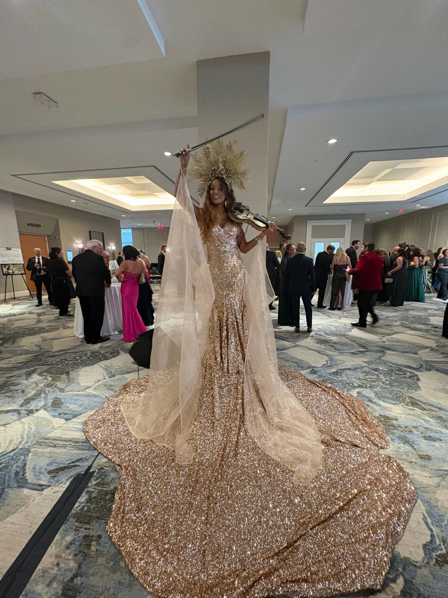 Person in a wedding dress with a long train, standing on a patterned carpet in an indoor setting.