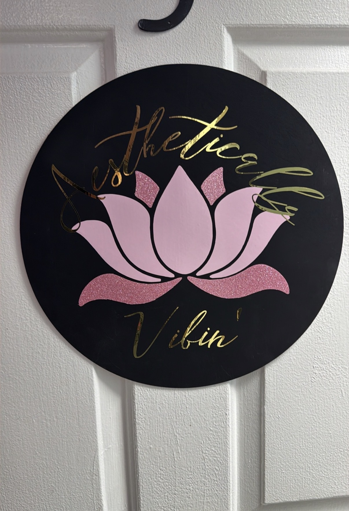 Round wall clock with a pink lotus flower and gold cursive text on a black background.