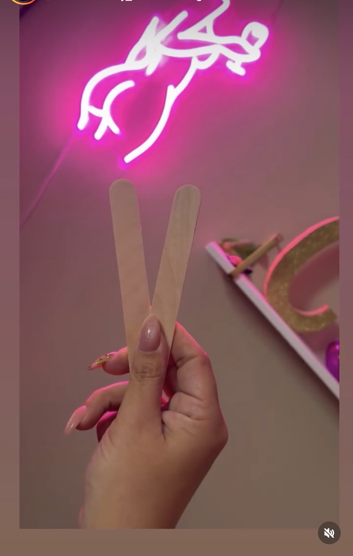 Hand holding two beige strips in front of a pink neon sign with Arabic script, and a pink and white object on a table.