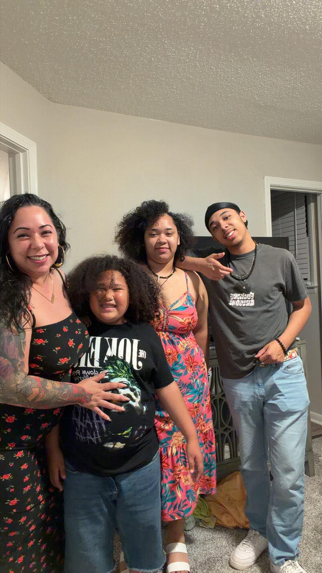 Four people standing indoors, smiling, with a window and a door in the background.