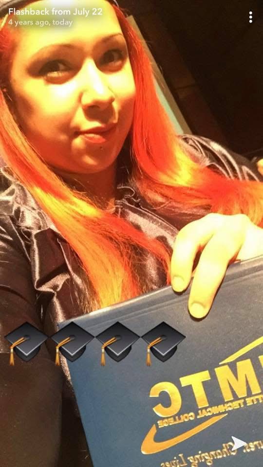 Young woman with red hair holding a blue box, smiling, indoors with warm lighting.