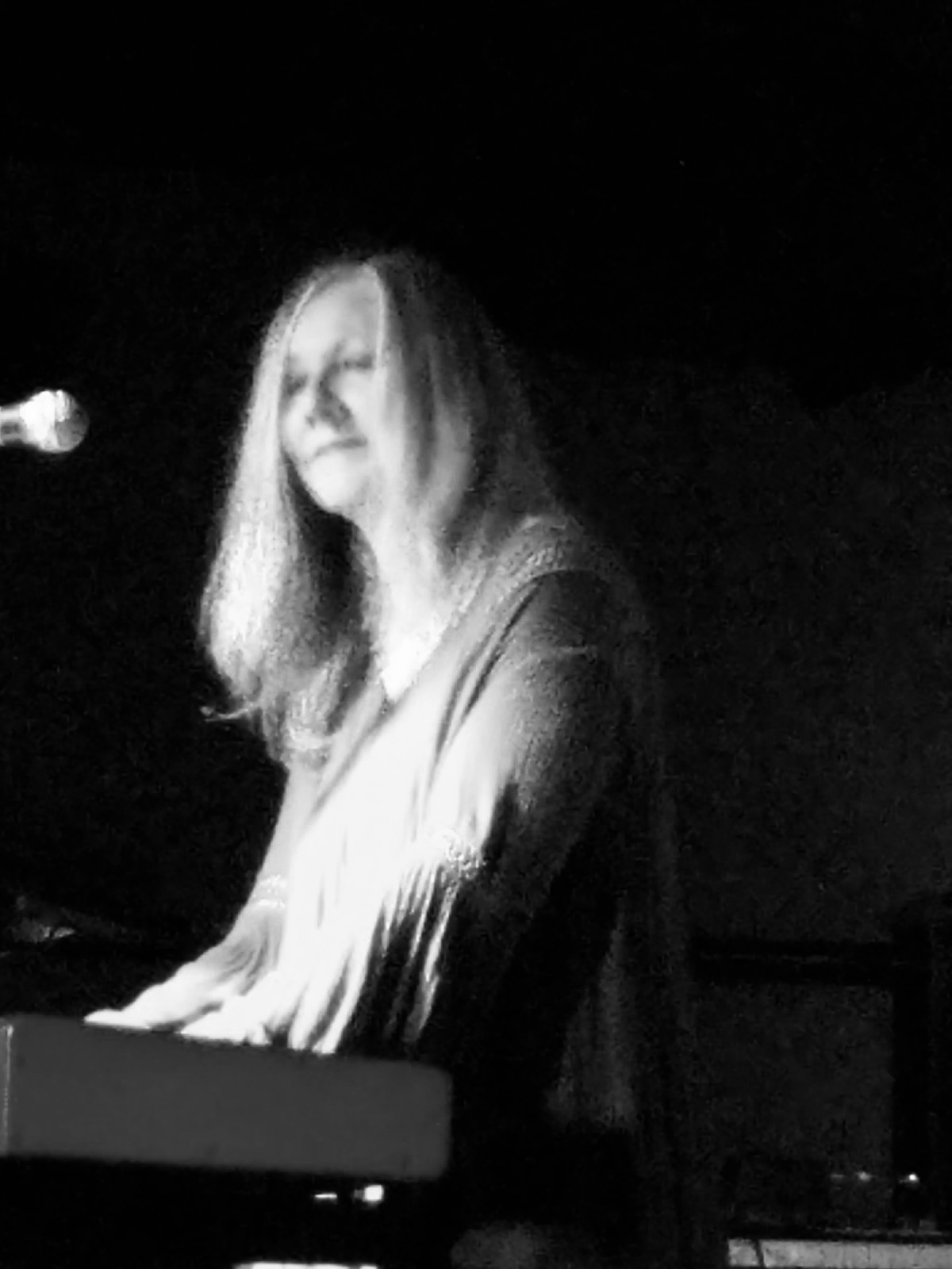 Person with long hair playing keyboard, smiling, in a dark setting.