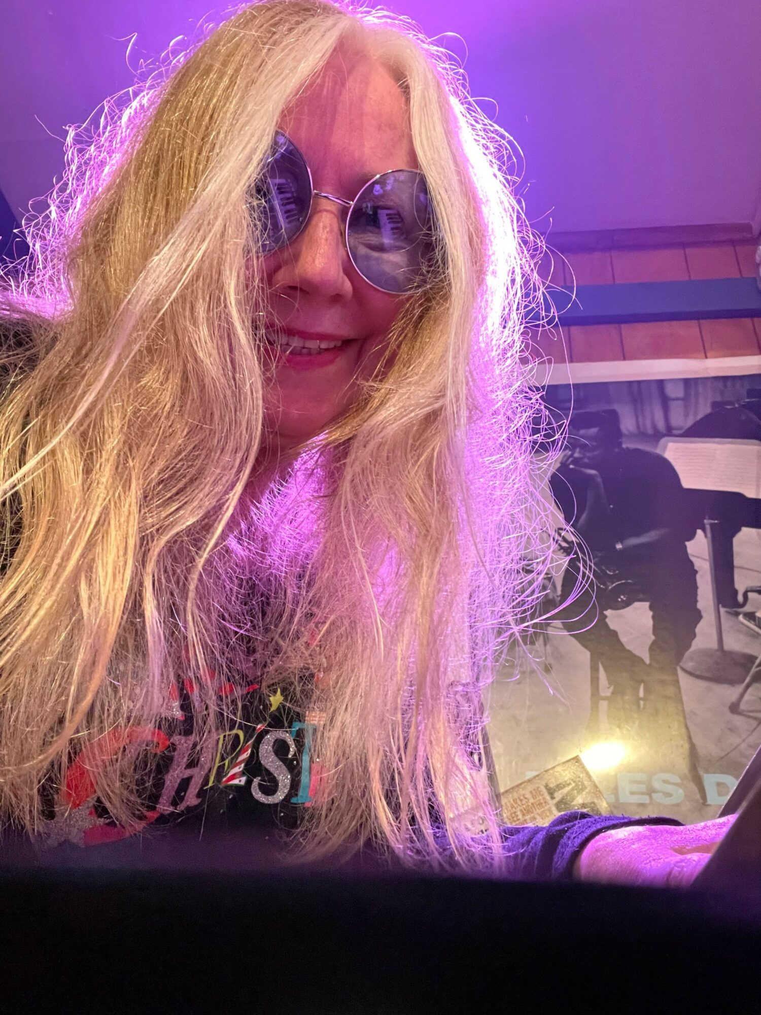 Person with long blonde hair and sunglasses, with purple lighting in the background.