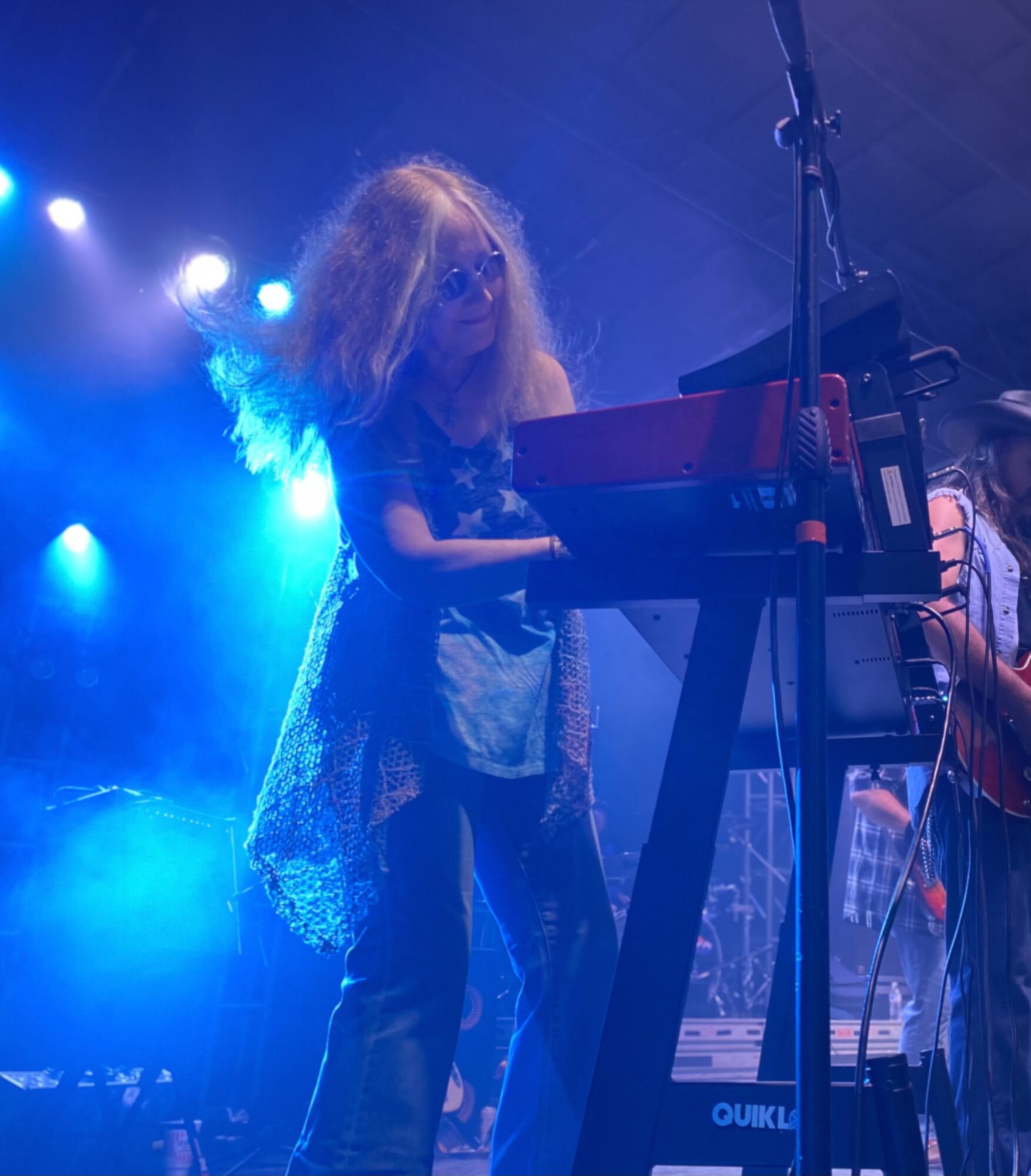 Child with curly hair playing a keyboard on stage with blue lighting.