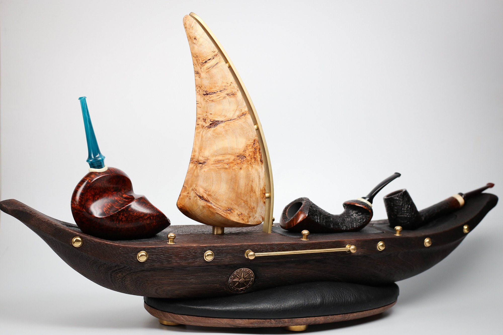 Decorative boat-shaped sculpture with a sail, pipes, and a small vessel, on a plain background.
