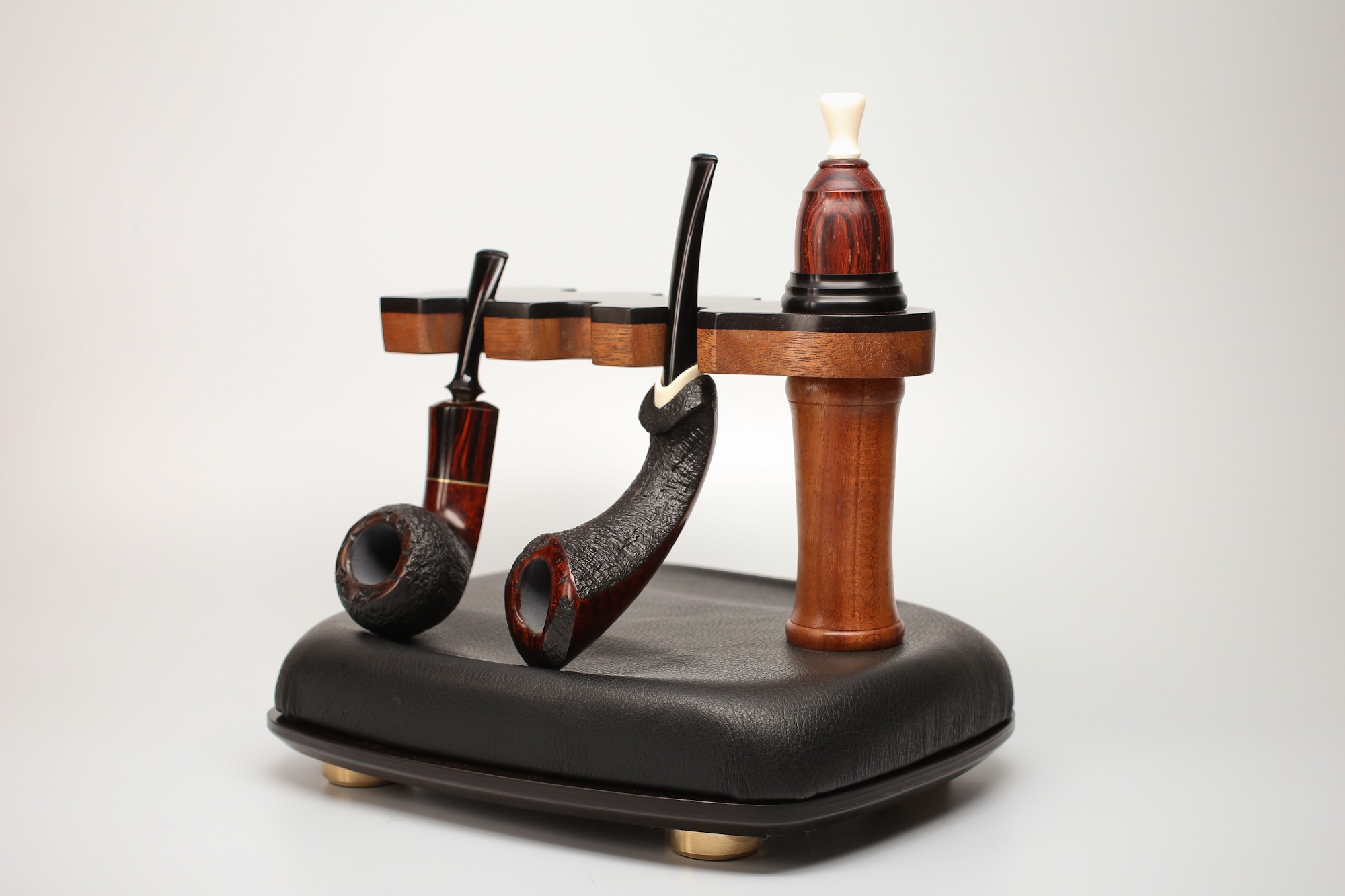 Two smoking pipes on a black cushion, with a small wooden stand holding a bottle of pipe tobacco, against a plain background.