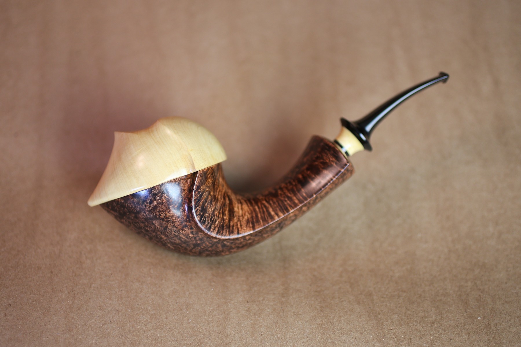 A smoking pipe with a curved brown wooden bowl, a light-colored stem, and a black mouthpiece on a wooden surface.