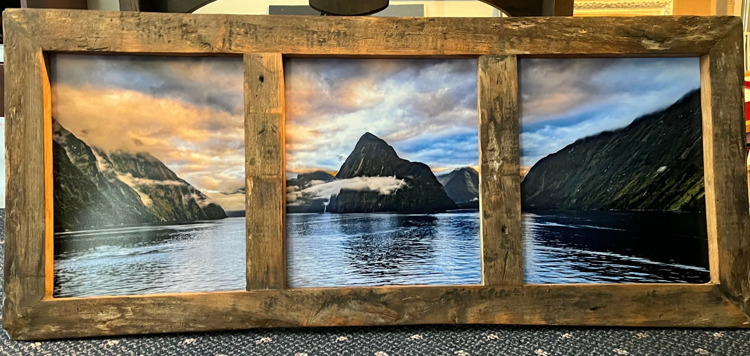 Framed landscape painting of a fjord with mountains and water, divided into four sections, with a cloudy sky.