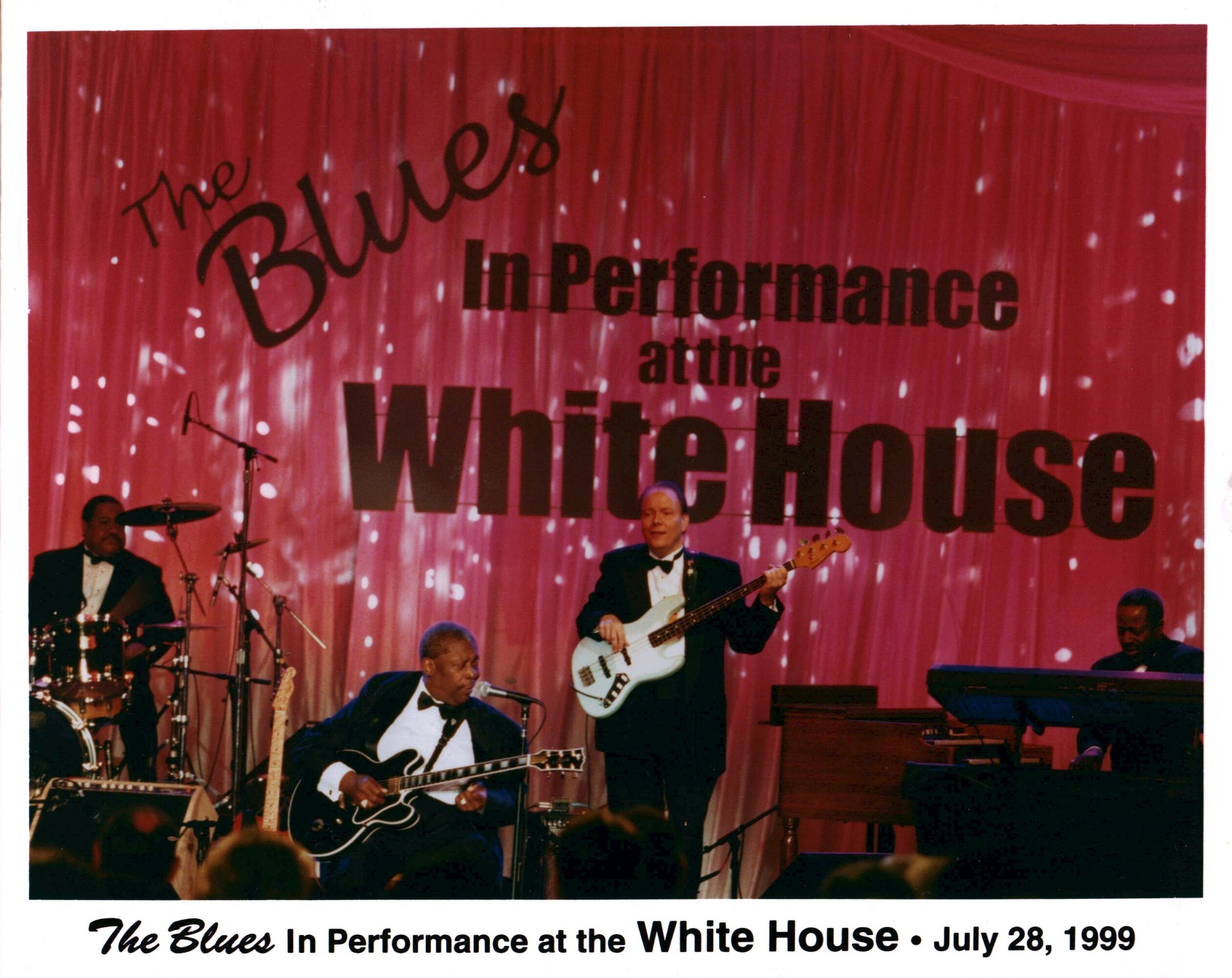 Band performing on stage with pink curtain background, text reads 'The Blues in Performance at the White House July 28, 1999'.