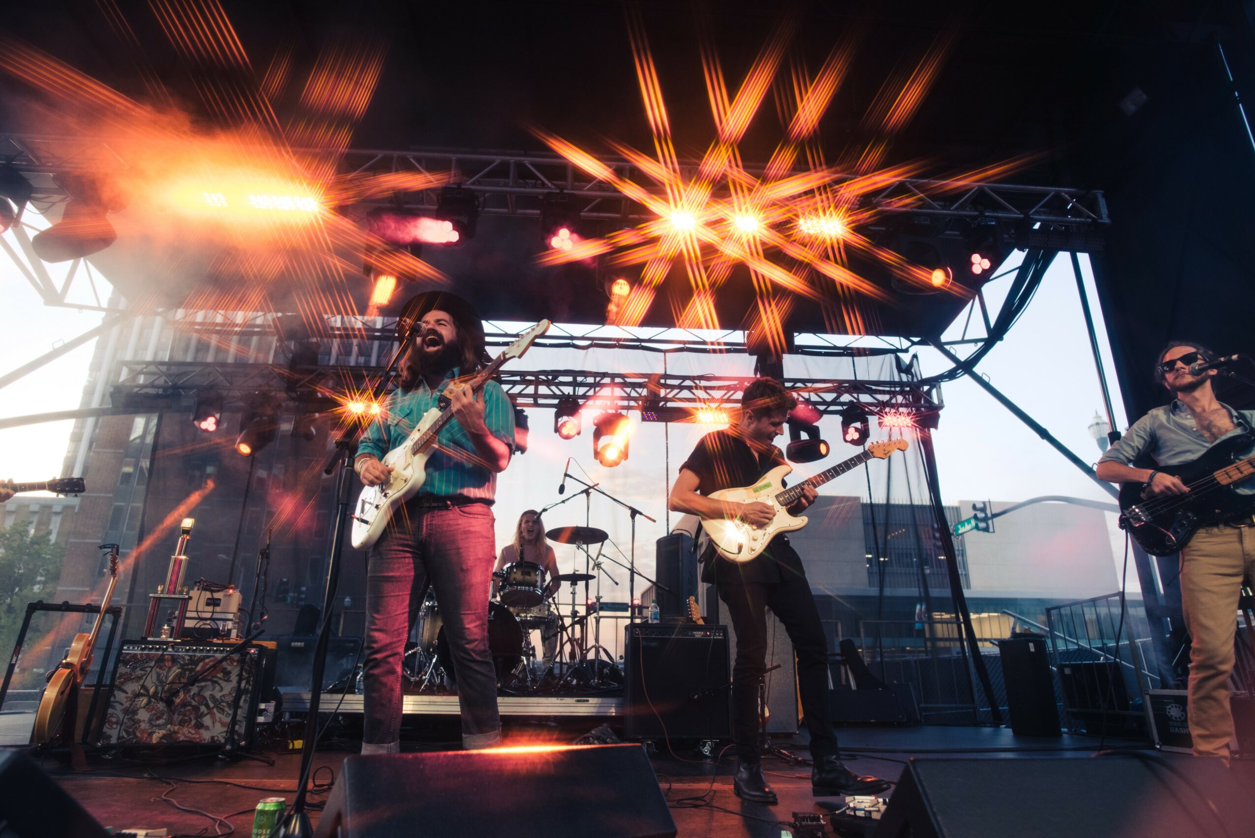 Band performing on stage with bright lights and musical instruments, audience visible in the background.