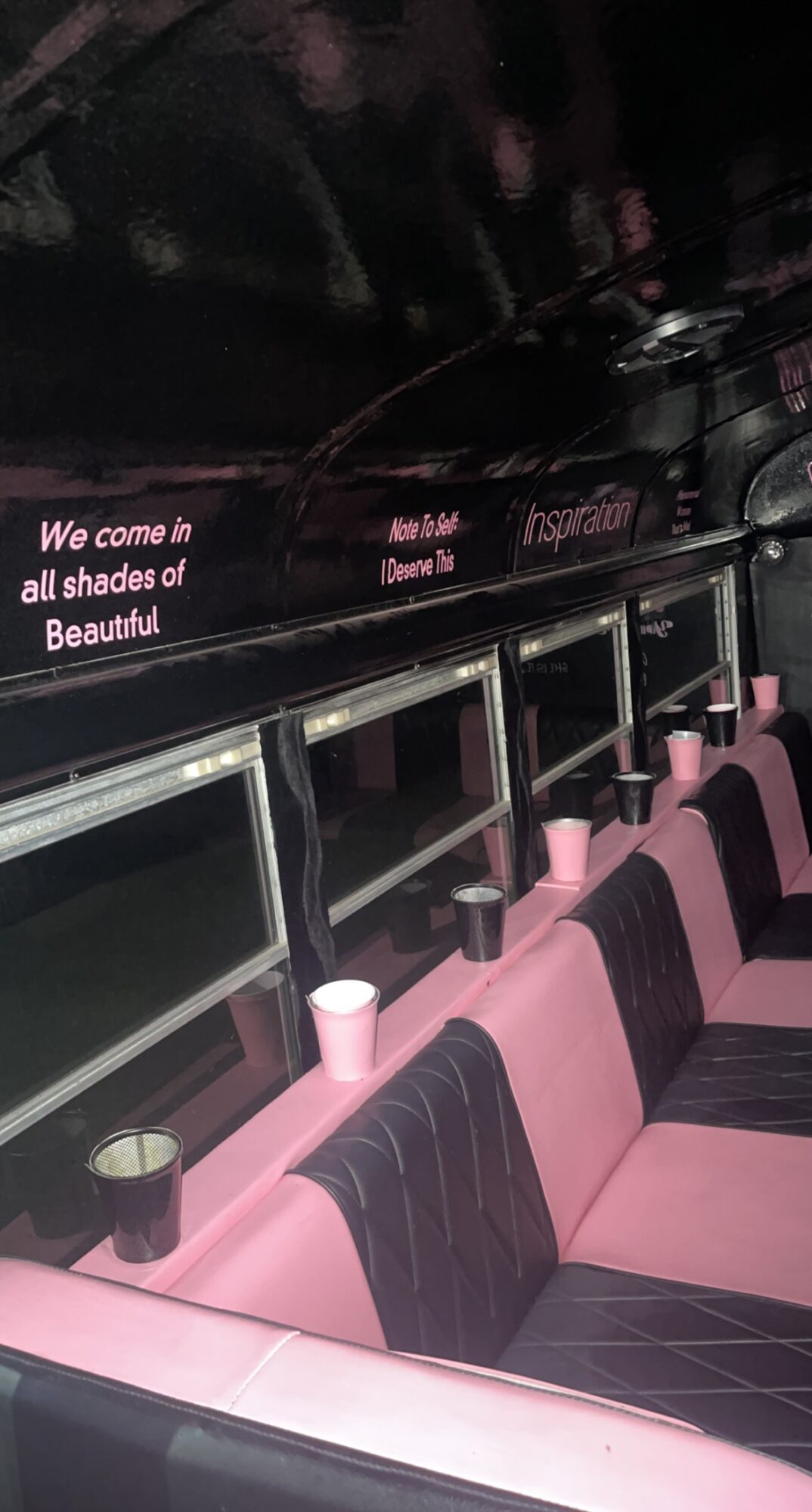 Bus interior with pink and black seats, cup holders, and a window with text about shades of beauty.