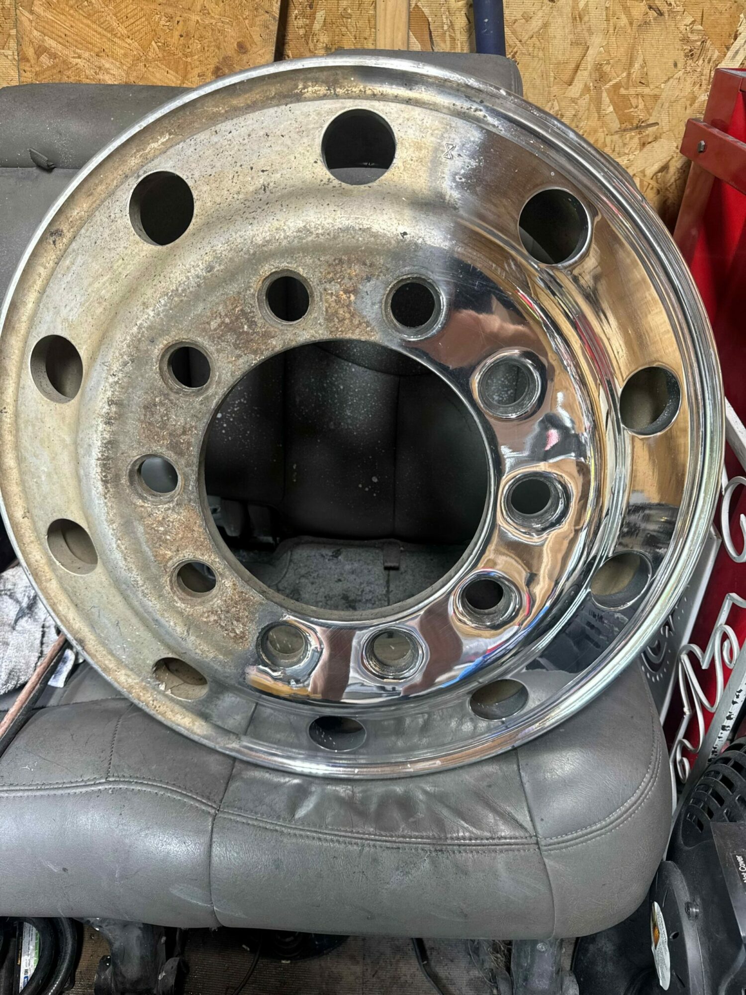 Metal wheel rim with multiple holes, placed on a gray surface, with a red object partially visible in the background.