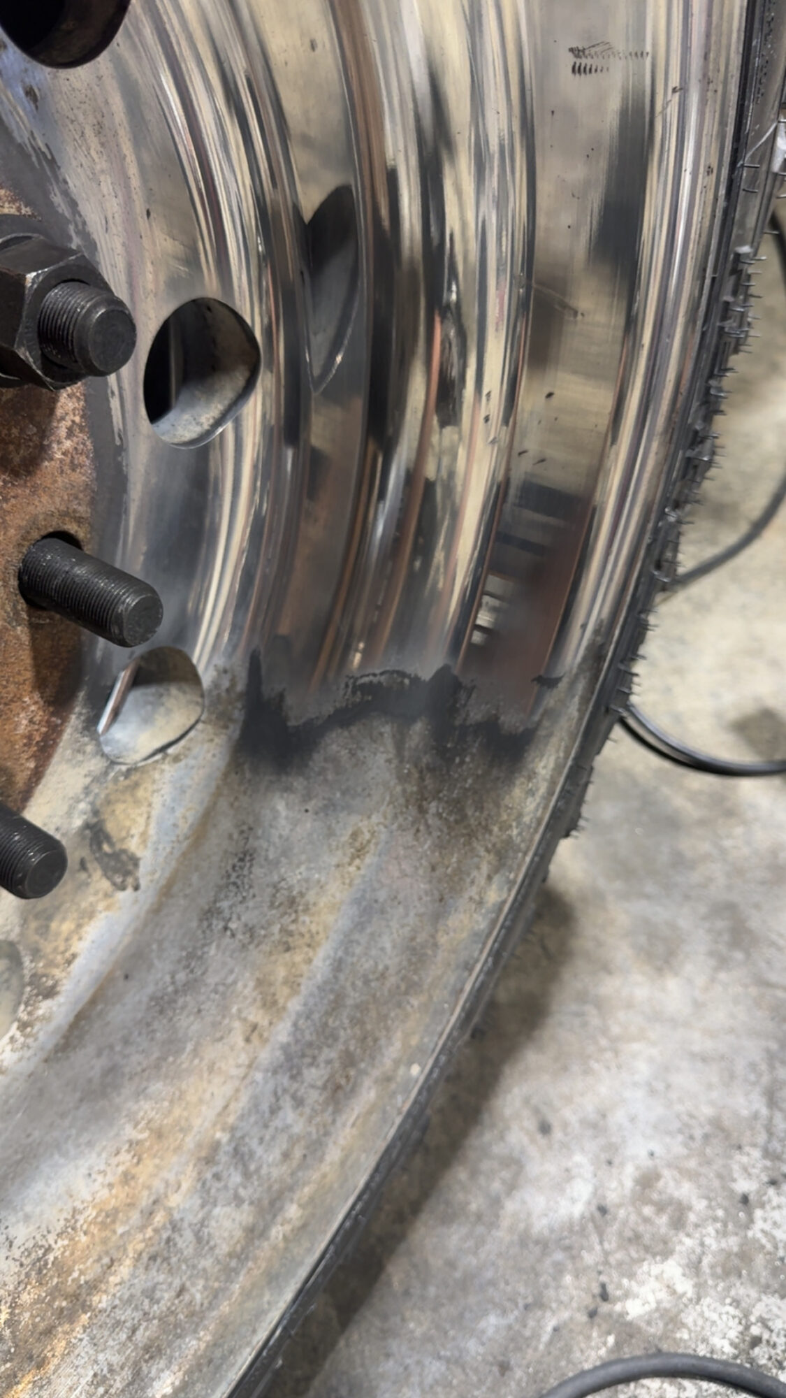 Close-up of a shiny metallic wheel rim with lug nuts, on a concrete surface.