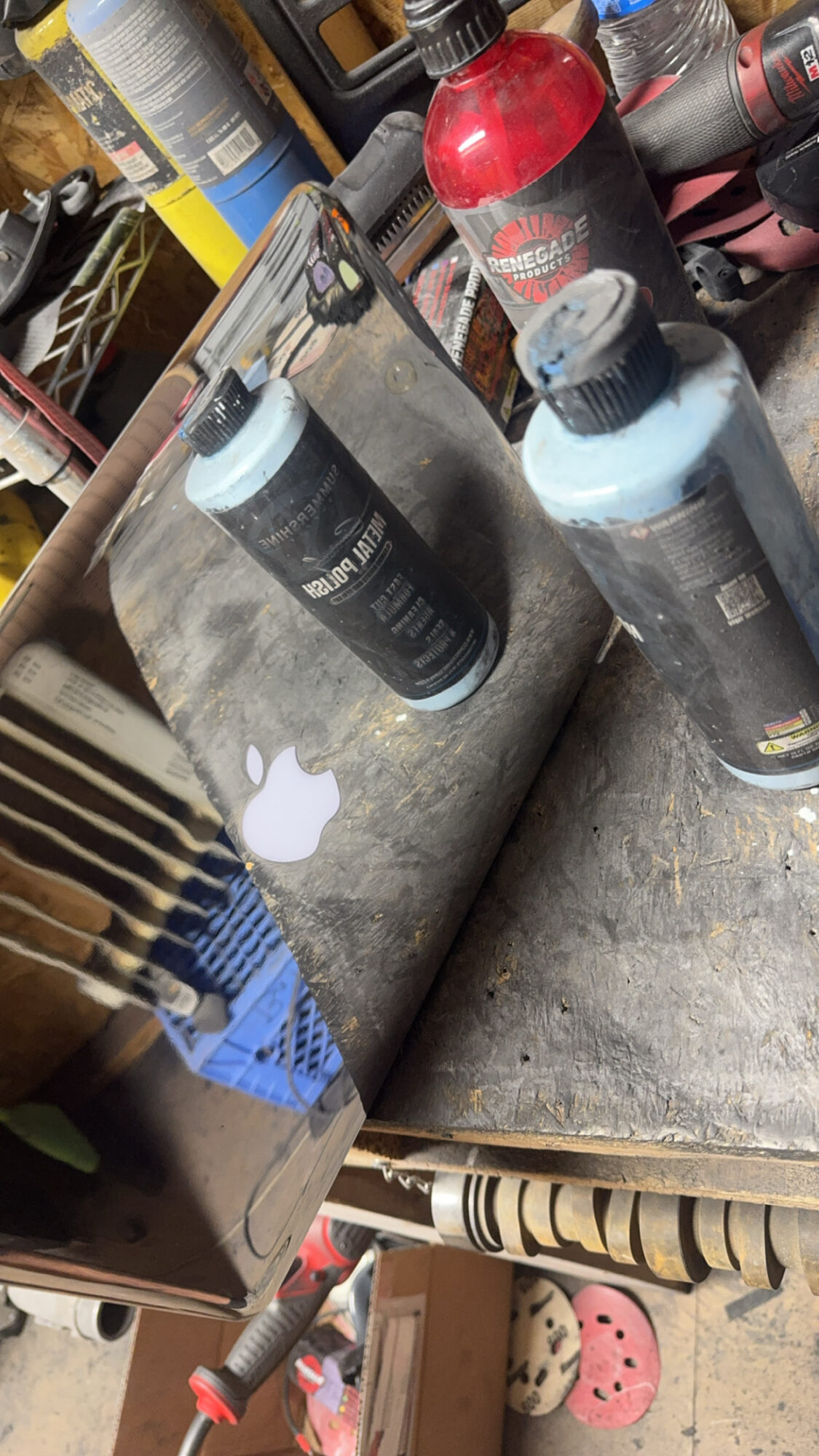 Laptop with Apple logo, two bottles of black and blue paint, and a red fire extinguisher on a workbench.