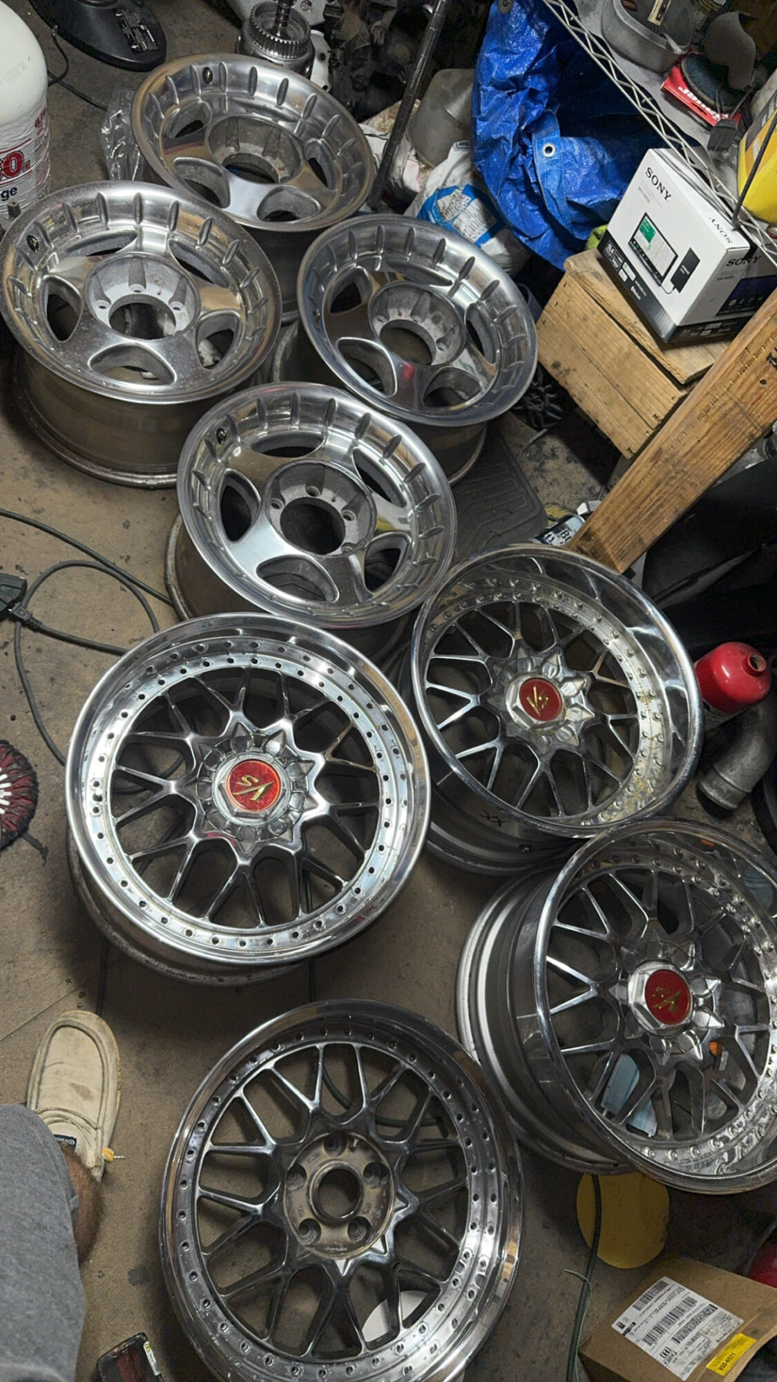 Multiple car wheels stacked and scattered in a cluttered workshop or garage.