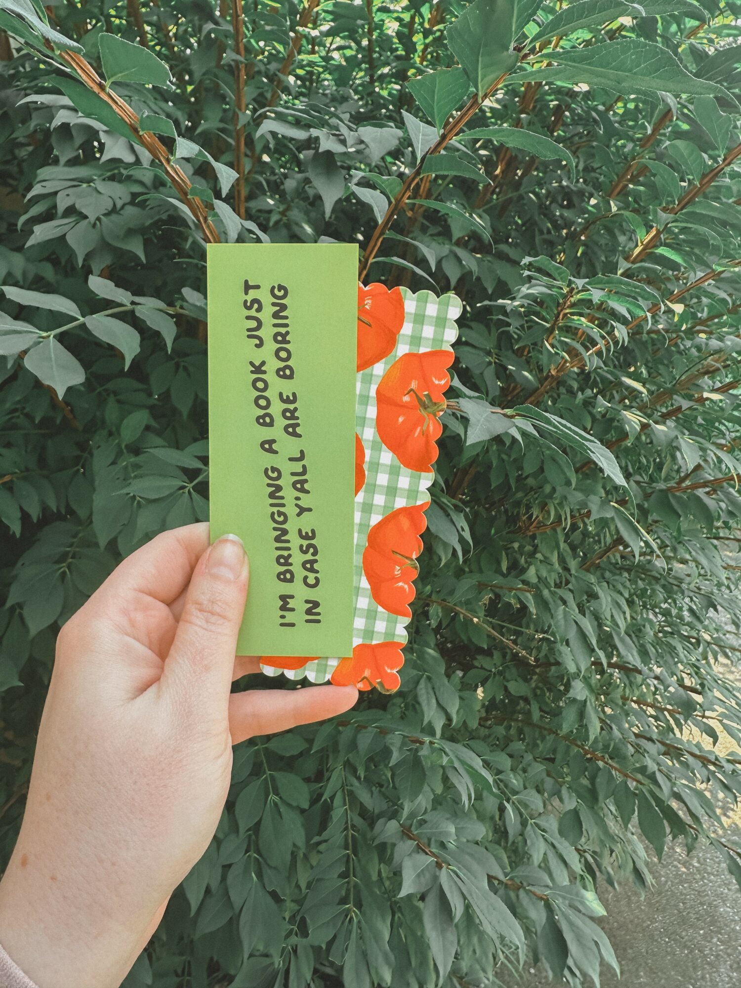 Hand holding a green tag with warning text, plant with green leaves in background.