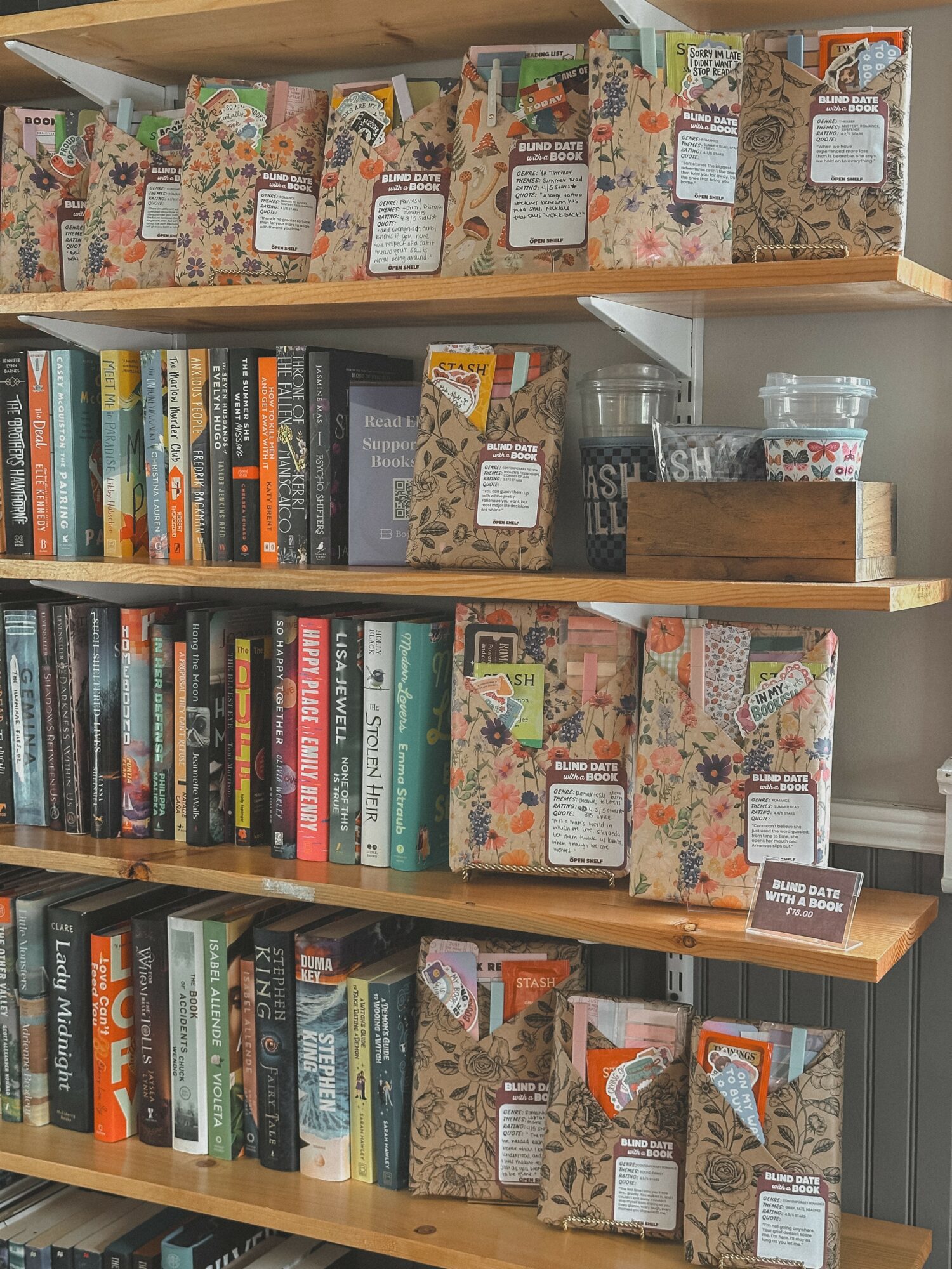 Bookshelves filled with books and decorative items, with patterned packages on top and middle shelves, and a small sign on the bottom shelf.
