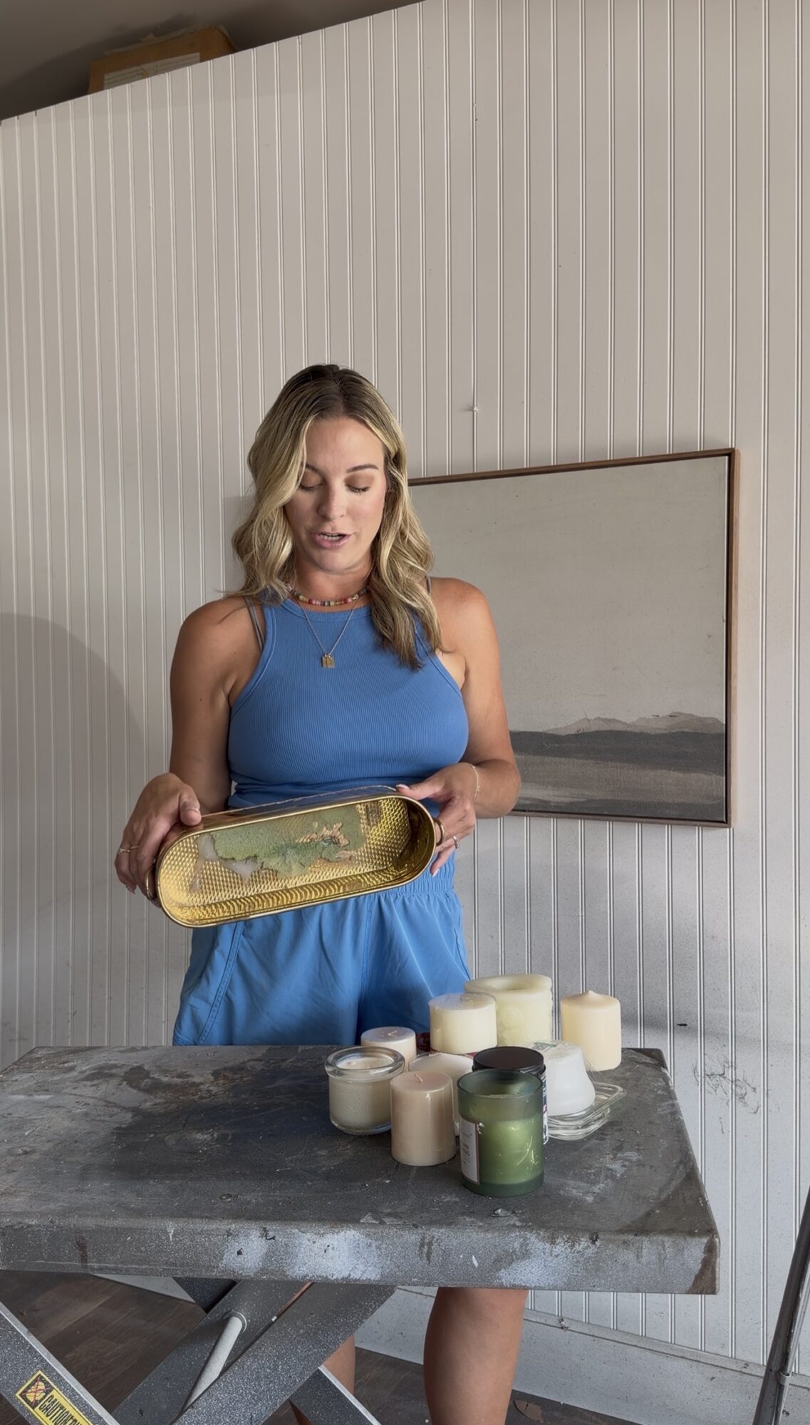 Woman in blue dress holding a tray, standing near a table with candles, in a room with white panel walls.