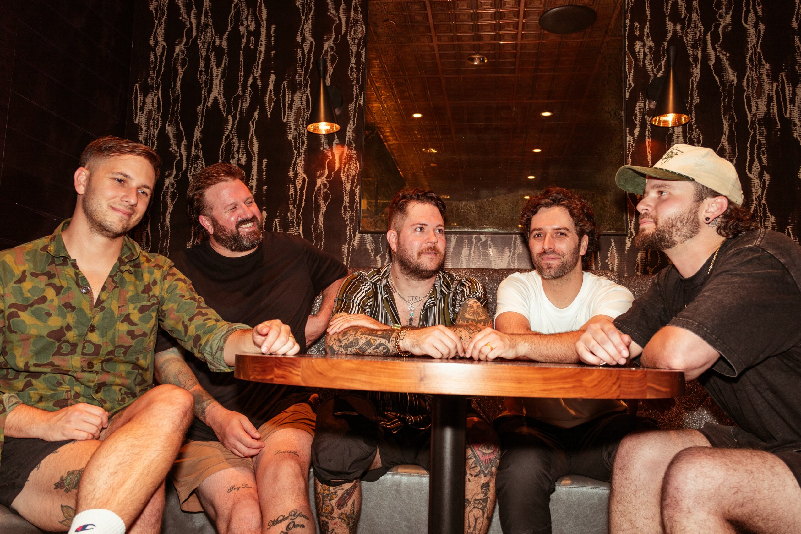 Five men sitting around a wooden table in a dimly lit room with waterfall decor, engaged in conversation.
