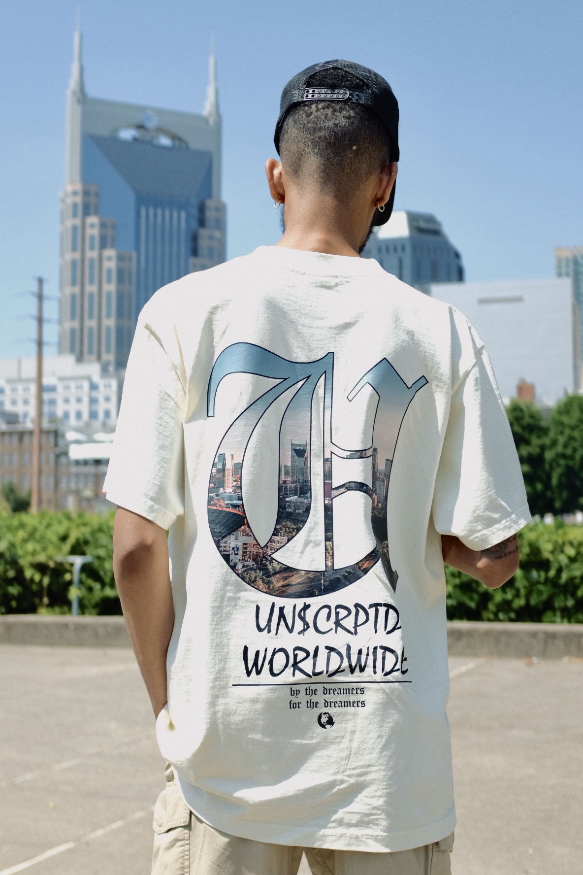 Person with short hair wearing a white T-shirt with a large graphic and text, city skyline in background