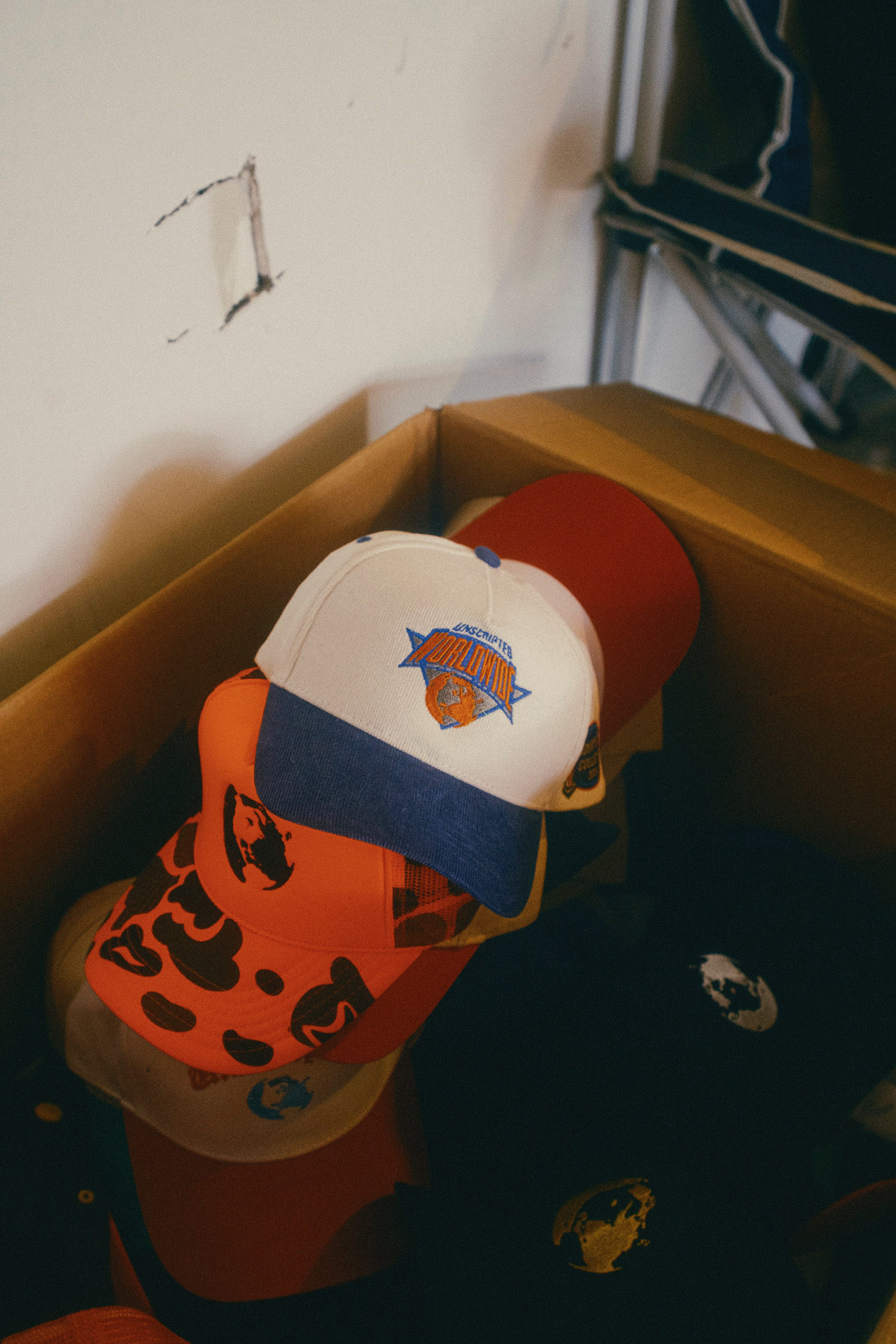 A white baseball cap with a logo, placed on a red object among other items in a box.