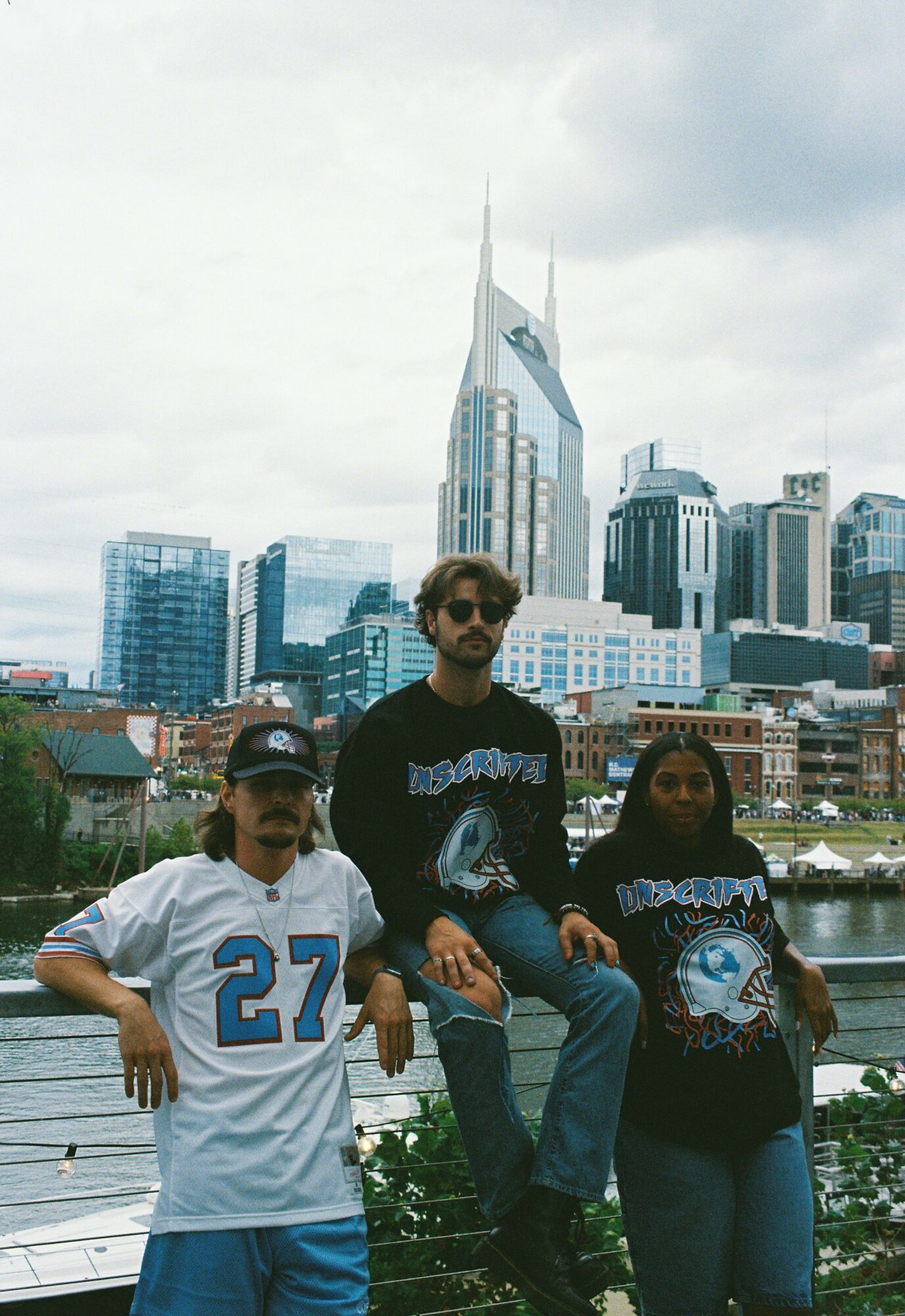 Four people standing on a rooftop with a city skyline in the background, including tall buildings and skyscrapers.