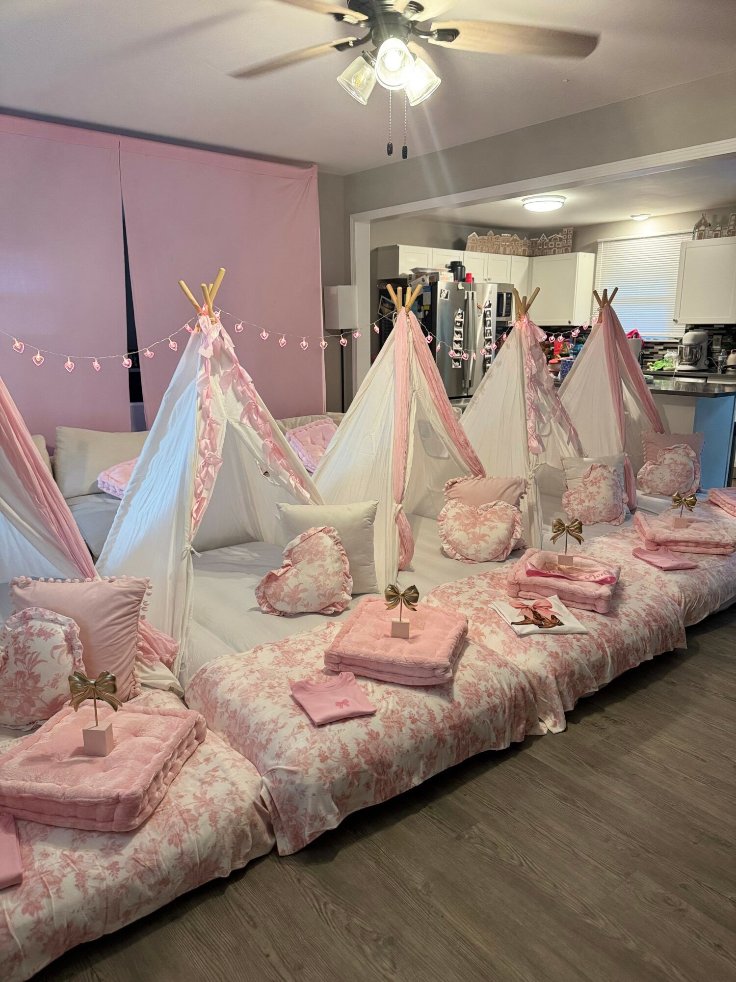 Multiple pink and white miniature tents with pillows and blankets arranged on a bed, decorated for a party or sleepover.