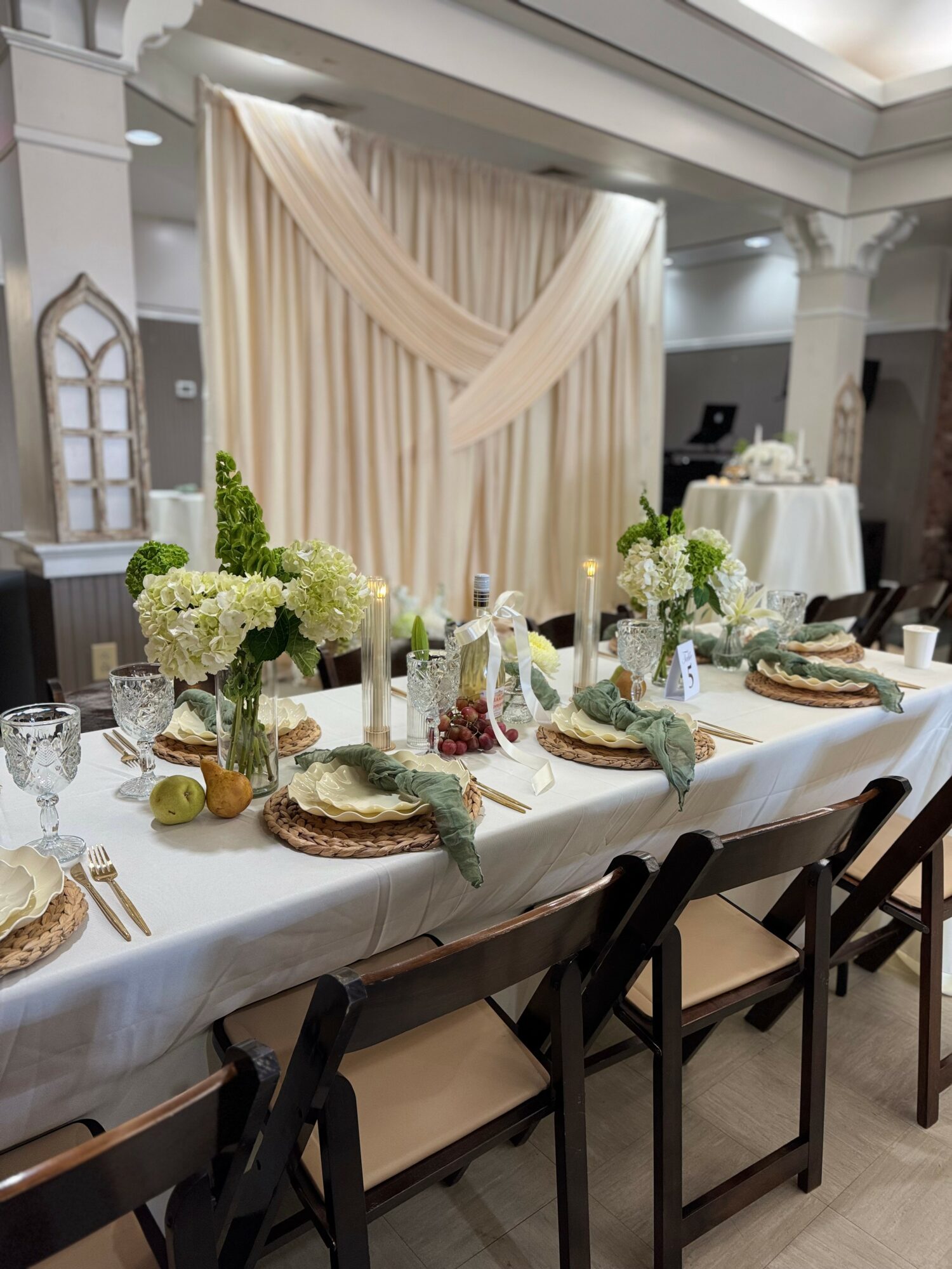 Elegant dining table with floral centerpieces, candles, and place settings in a decorated room with draped curtains and arches.