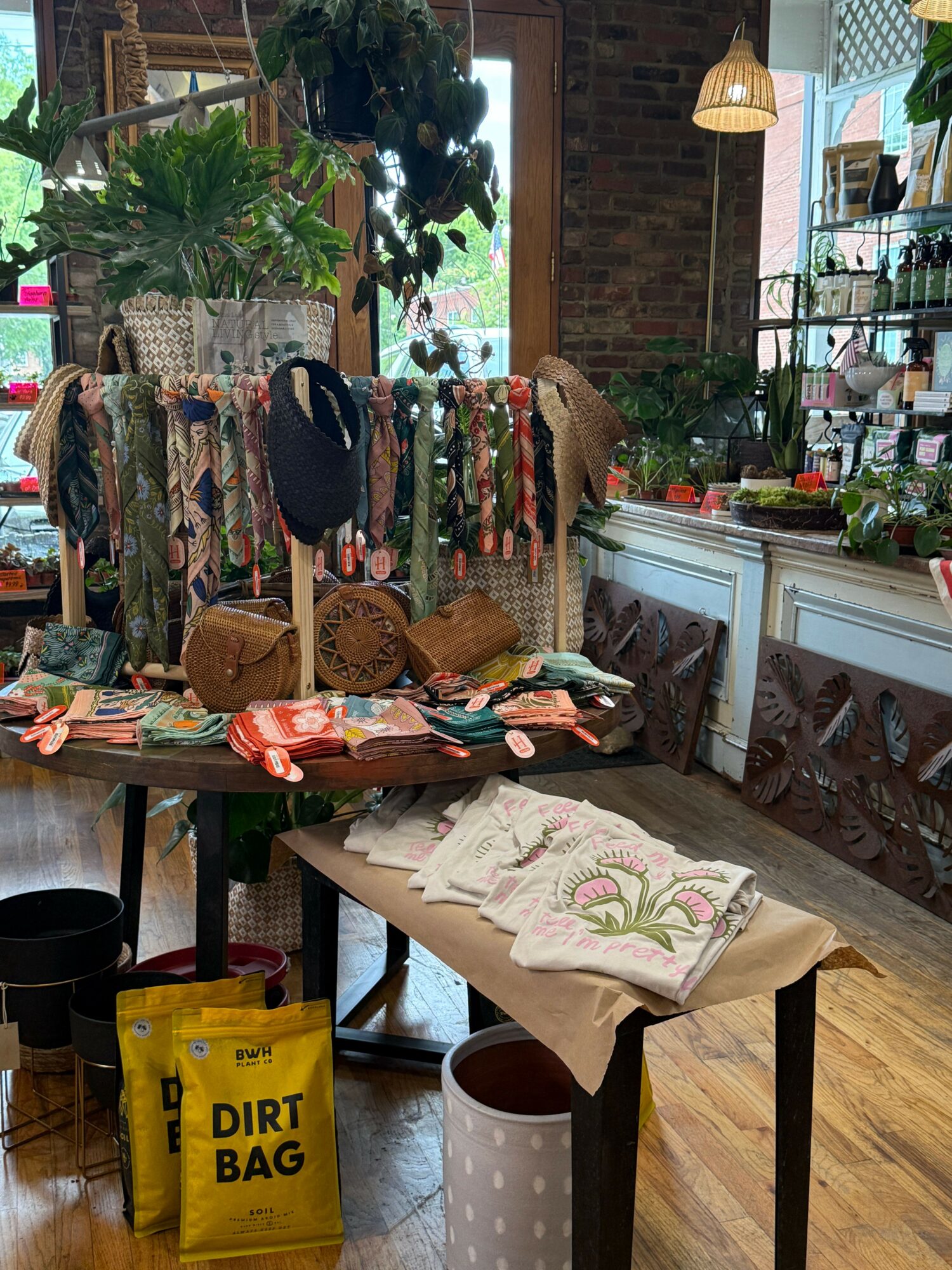 Clothing rack with colorful garments, a table with fabric and sewing supplies, and a window with plants and outdoor view.