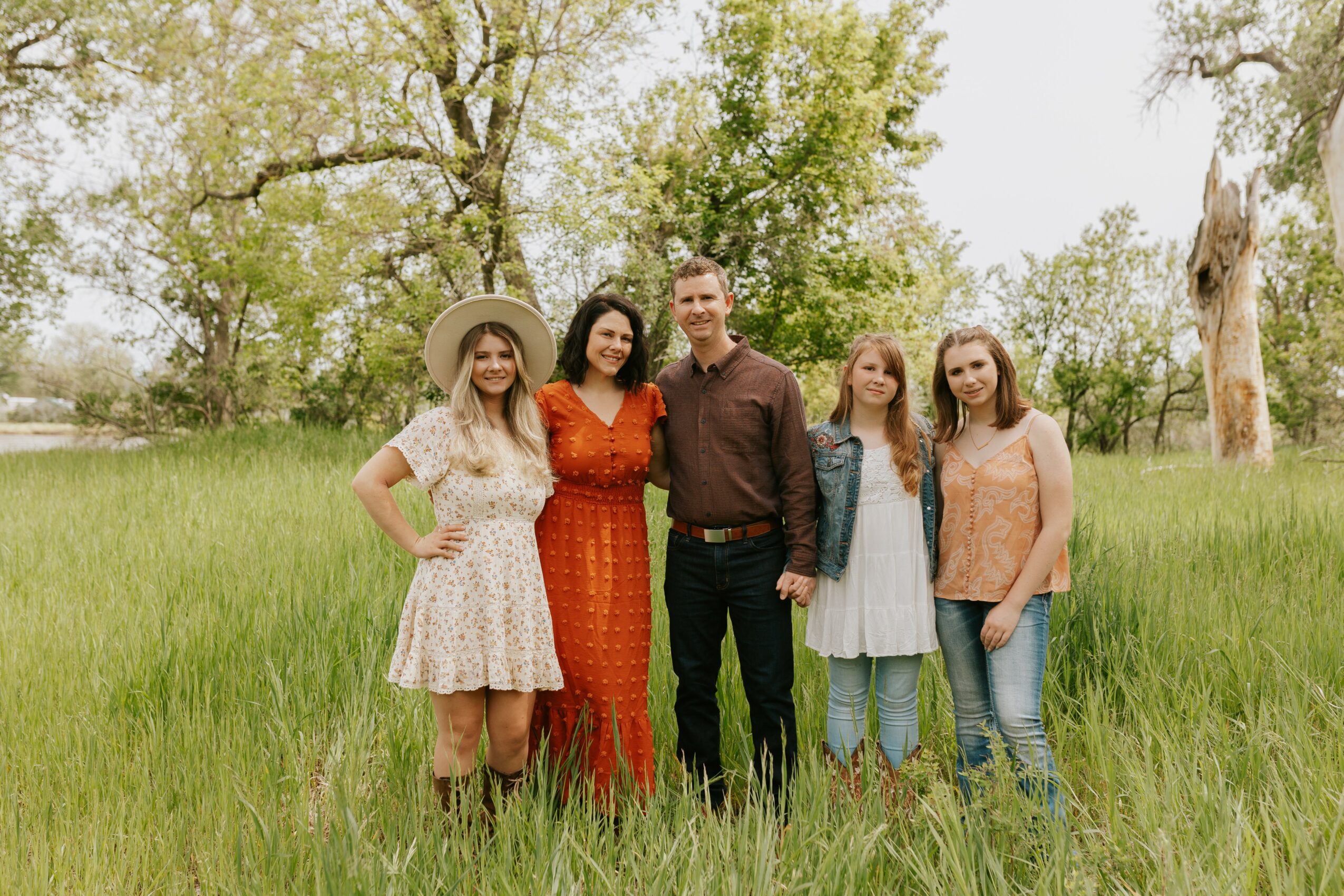 Group of five people standing in a grassy field with trees in the background, smiling at the camera.