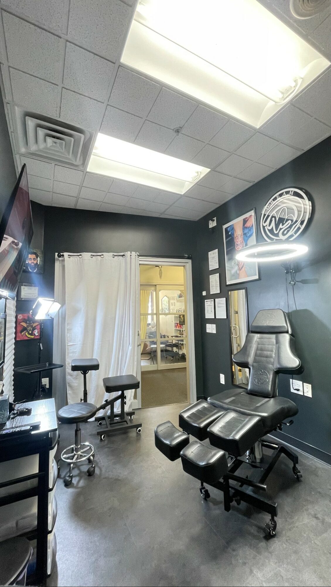 Medical examination room with chair, monitor, and medical equipment, illuminated ceiling lights, and a door with a curtain.