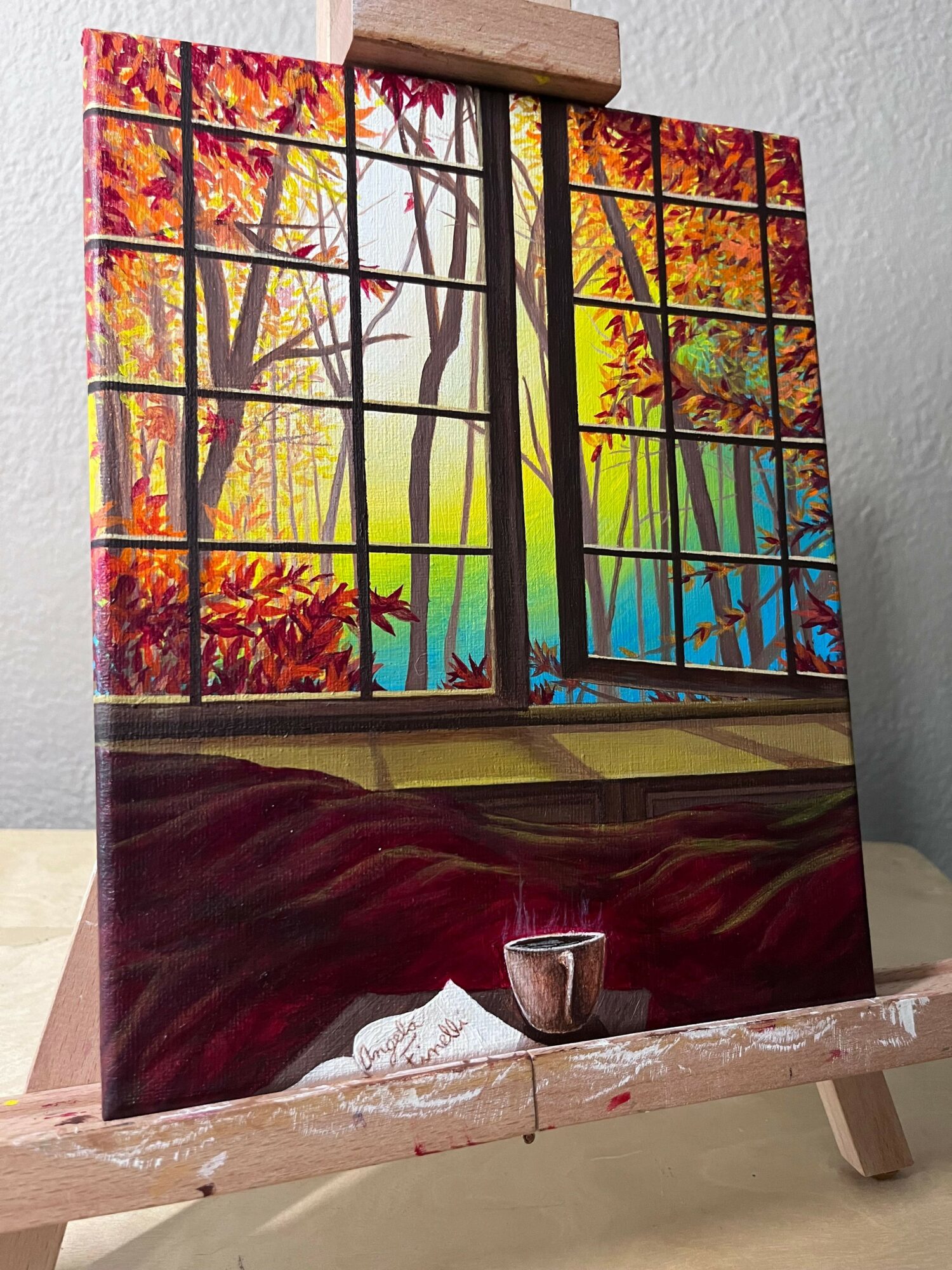 Colorful landscape painting of trees and sky, with a red and black abstract base, on a wooden easel.