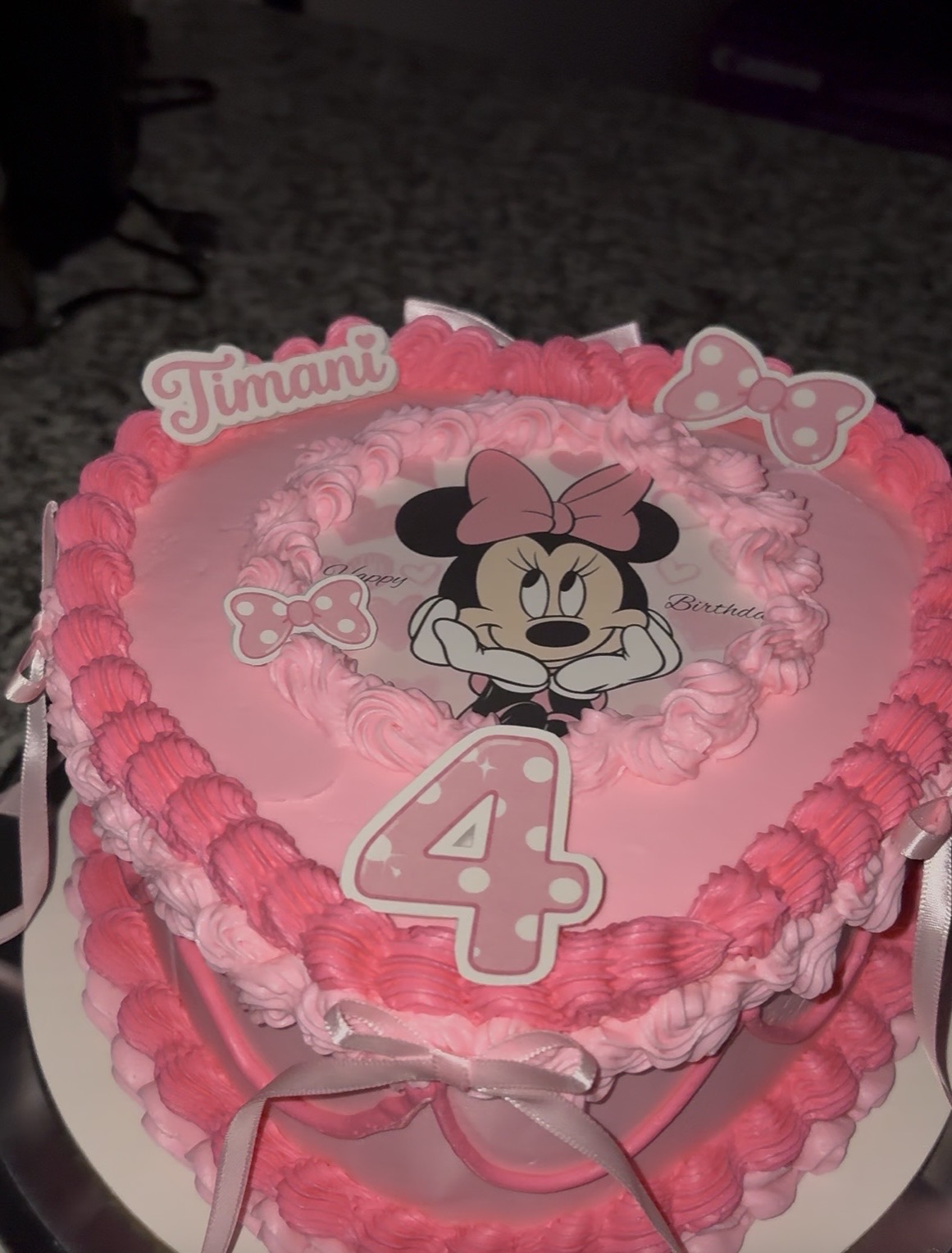 Heart-shaped birthday cake with pink frosting, Minnie Mouse image, number four, and decorative elements, on a white base.