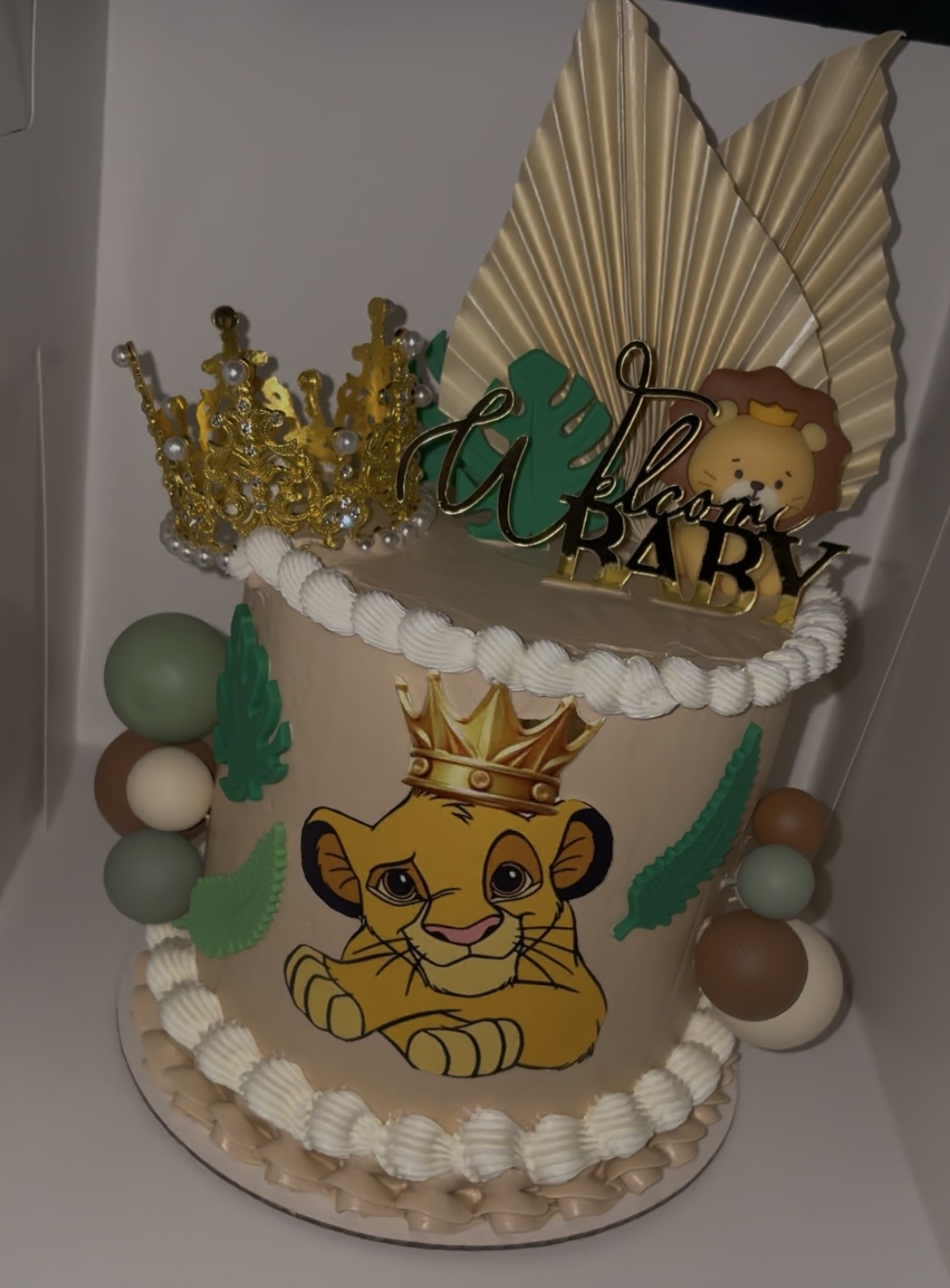 Decorative cake with lion illustration, gold crown, green and beige accents, and a 'Baby' sign, celebrating a child's birthday.