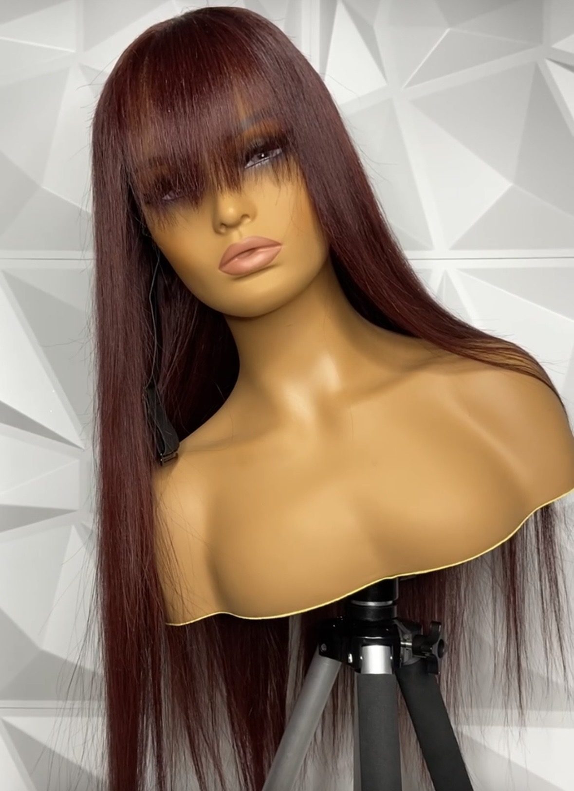 Mannequin with long, straight, reddish-brown hair and bangs, against a geometric white background.