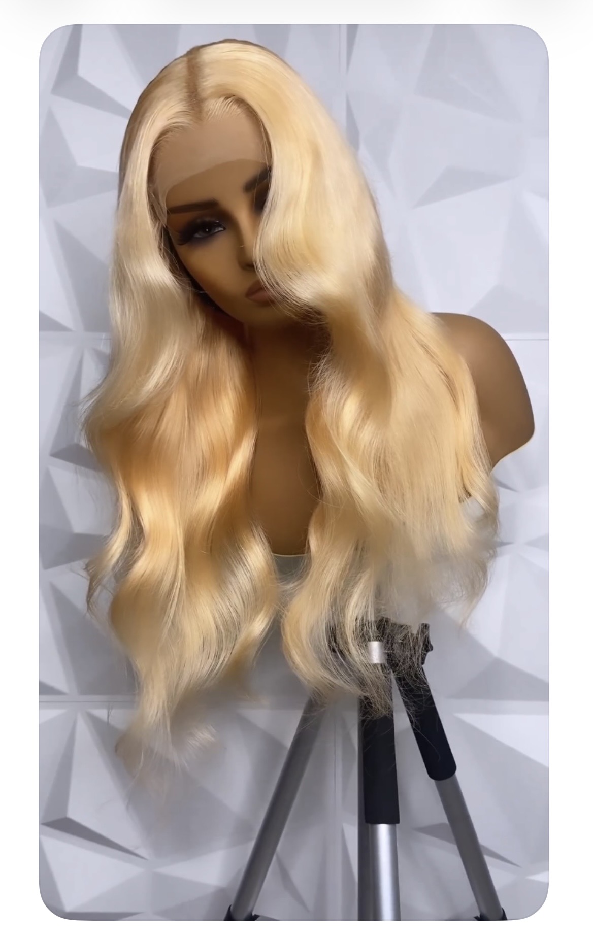 Blonde mannequin head with long wavy hair on a stand against a geometric background.