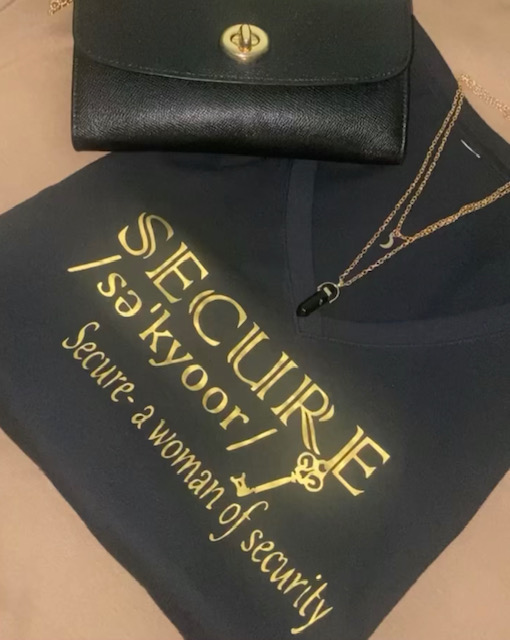 Black wallet with gold emblem, gold necklace with pendant, and a black cloth with gold text about security and women.