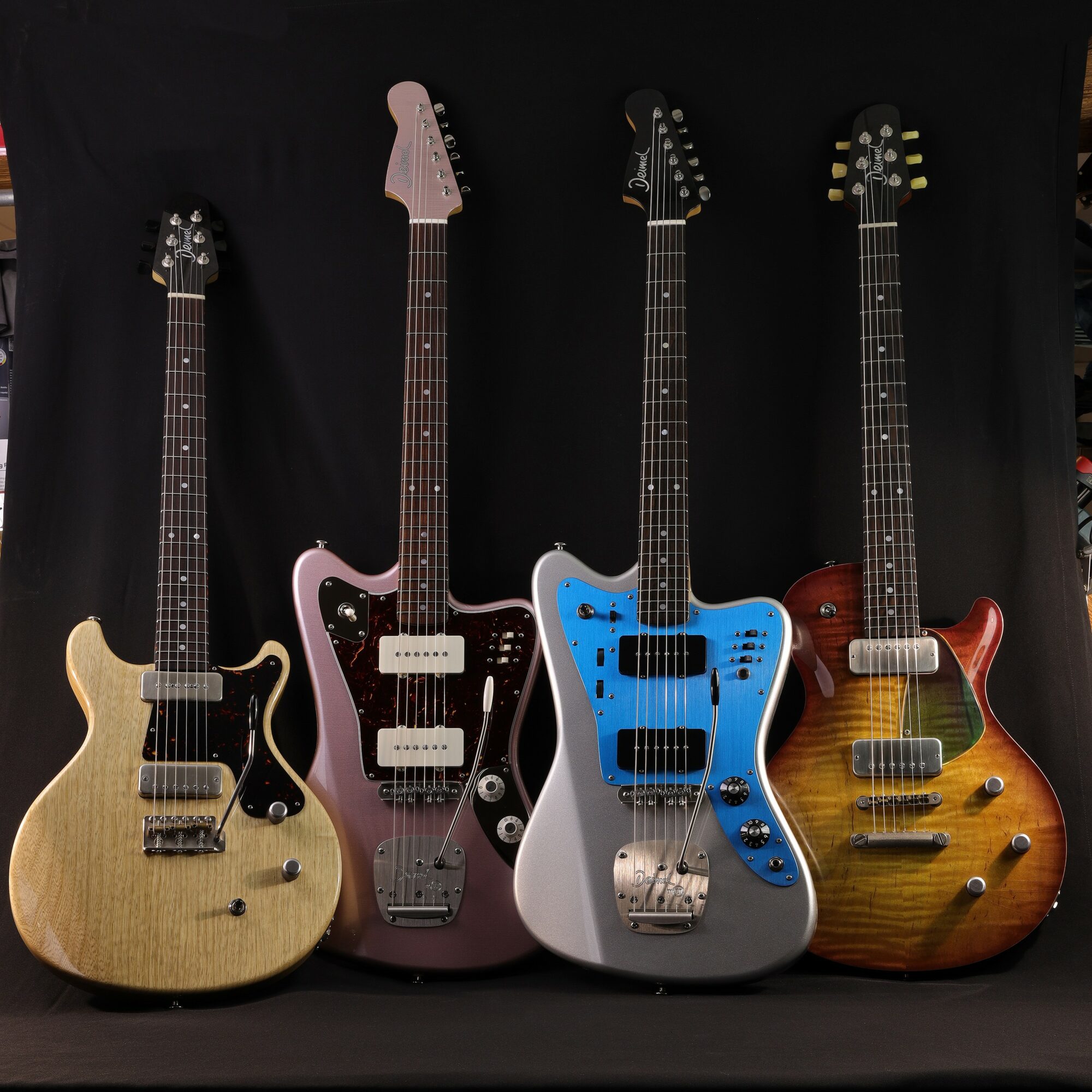 Four electric guitars with different colors and designs are displayed against a black background.