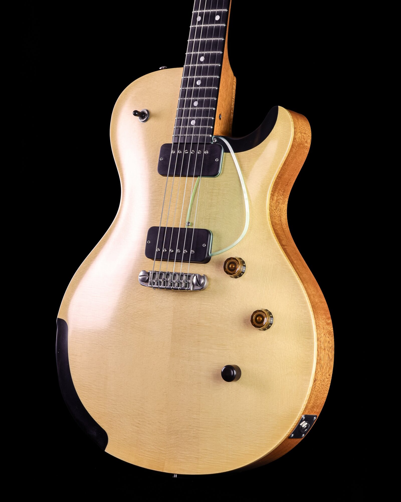 Electric guitar with a light wood finish, black pickups, and control knobs, against a black background.