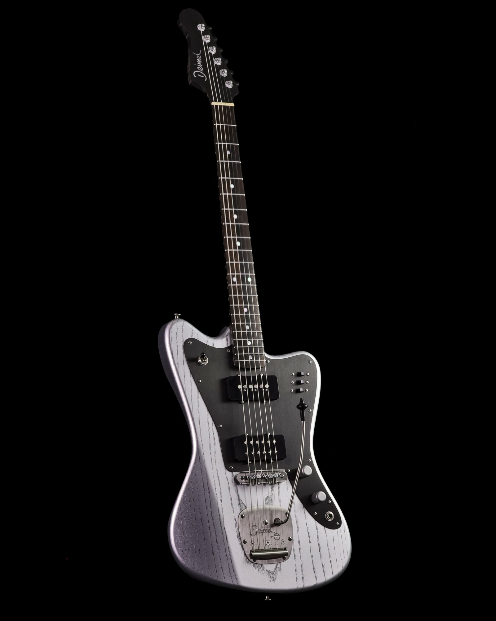 Electric guitar with a silver body, black pickguard, and multiple control knobs, set against a black background.