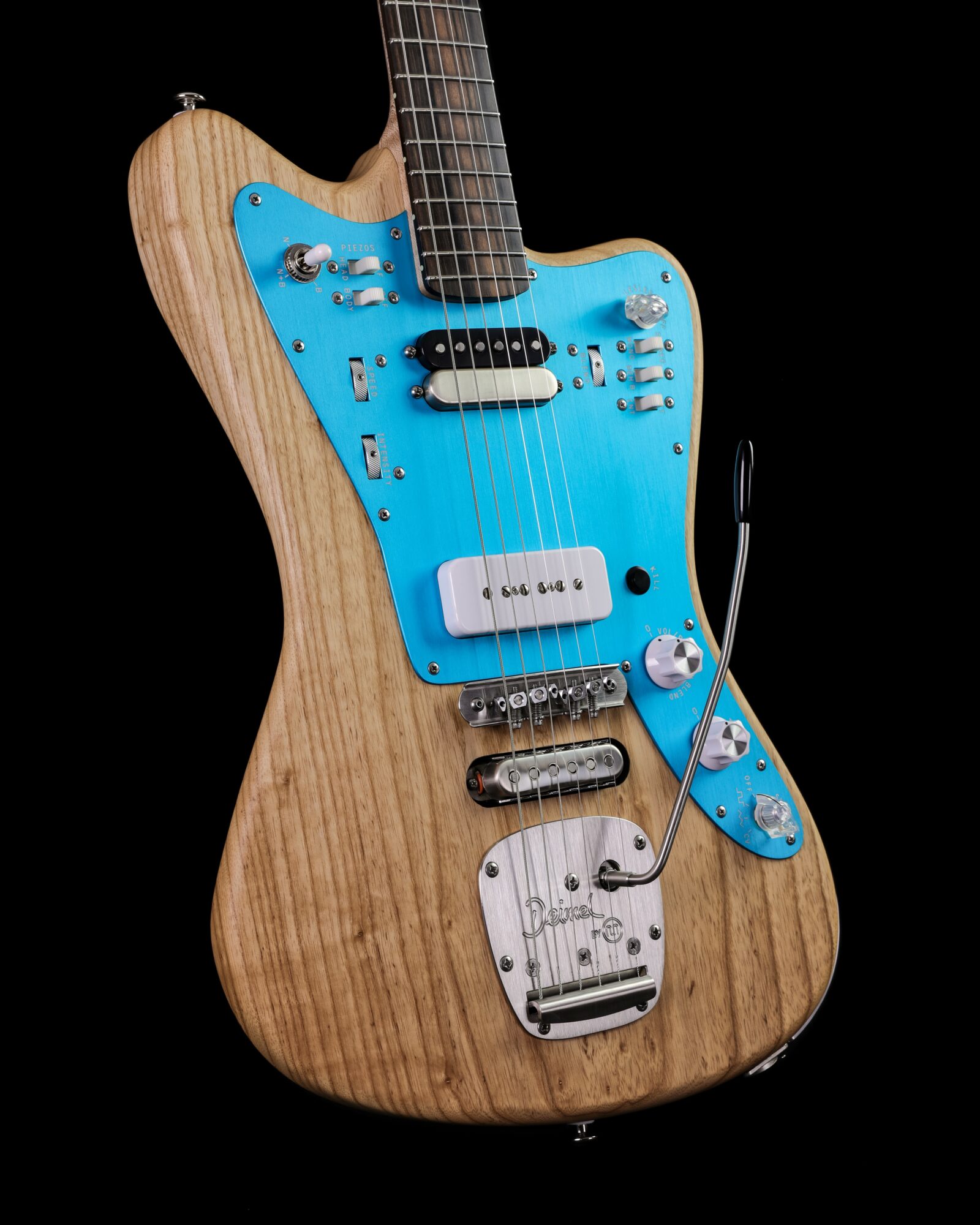 Electric guitar with a natural wood finish, blue pickguard, and various control knobs and switches, against a black background.