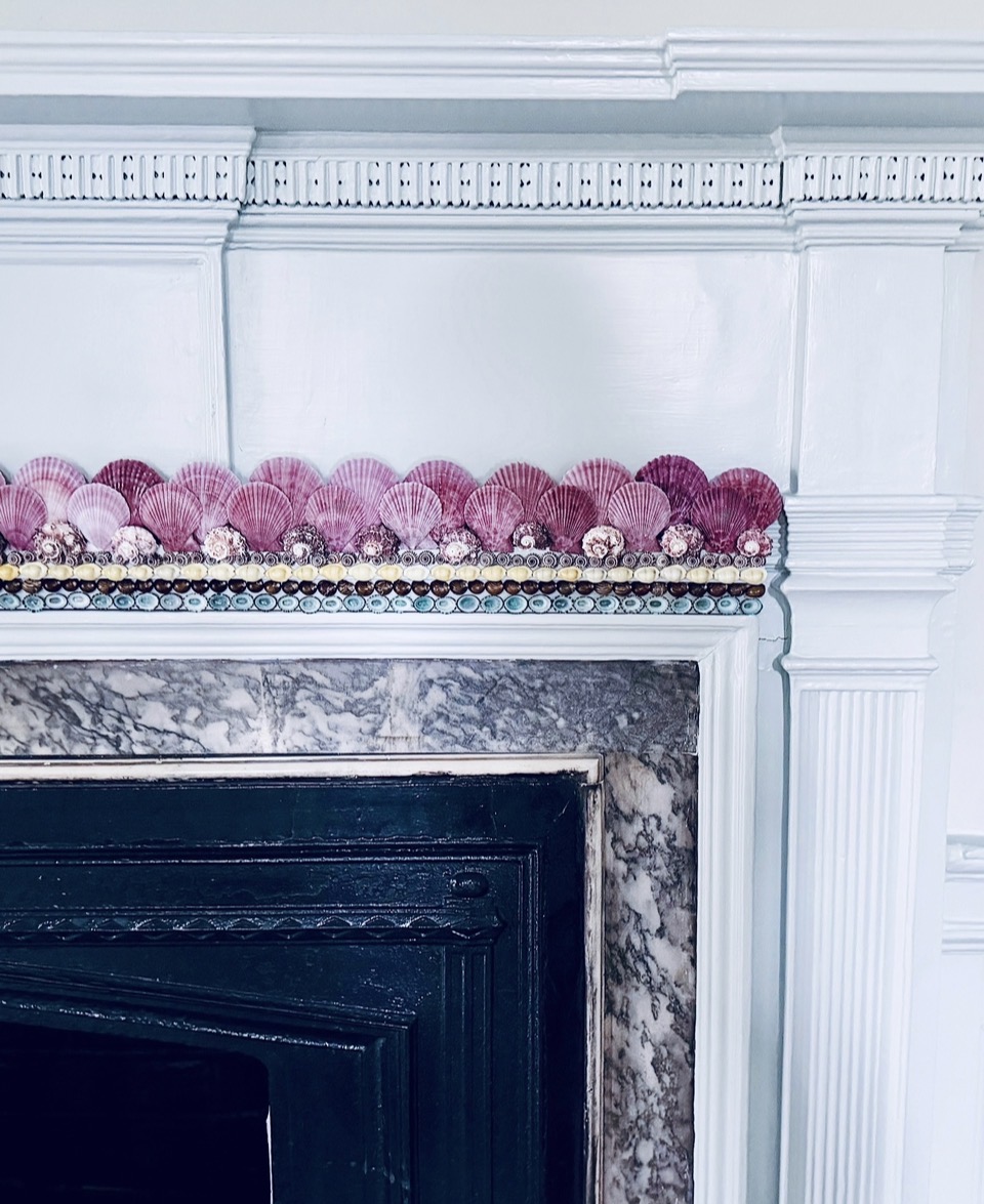 Close-up of a decorated fireplace mantel with pink and purple decorative balls, marble surround, and white ornate molding.