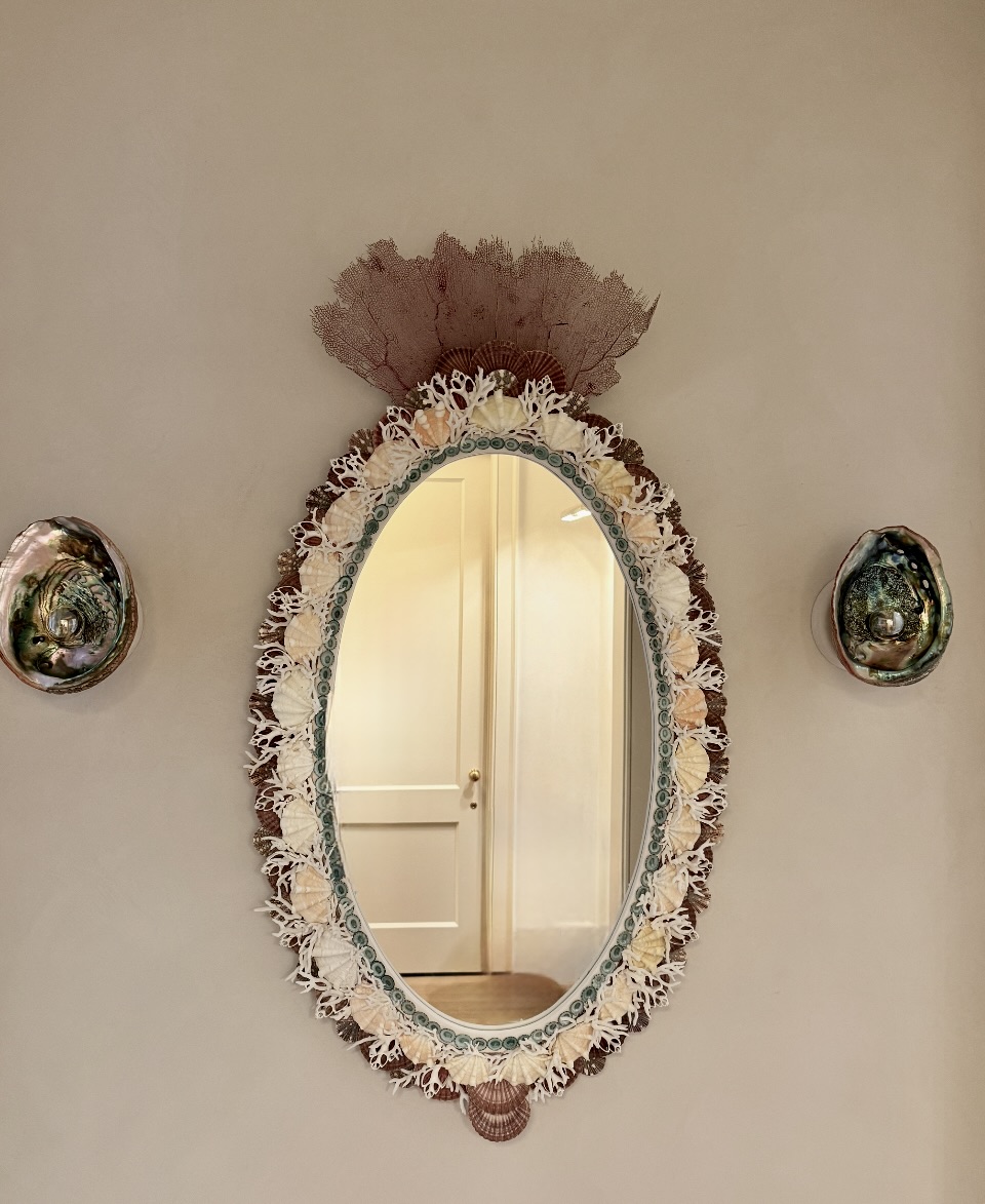 Oval mirror with decorative frame on wall, flanked by two small round mirrors, door reflected in mirror, neutral background.