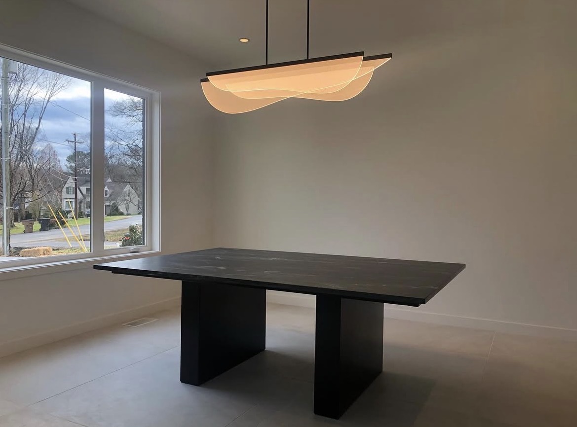 Dining room with a large window, a black table, and a modern hanging light fixture.