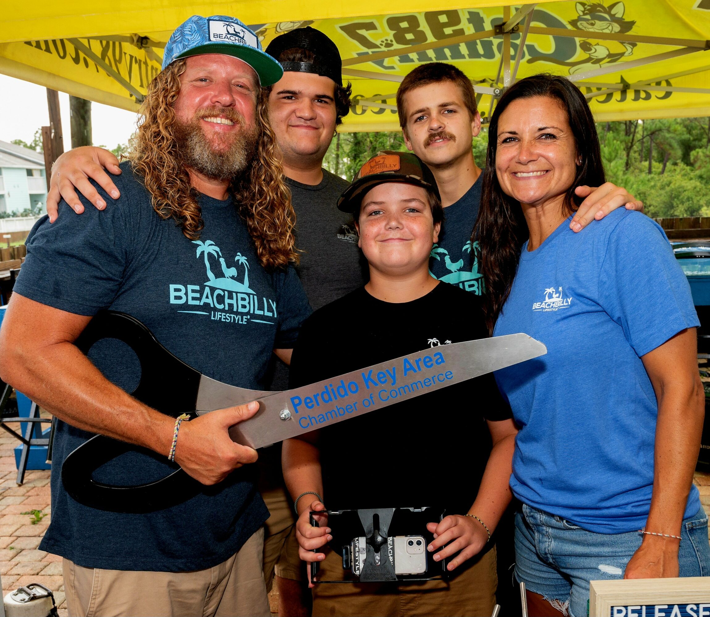 Group of five people smiling outdoors, holding a key with a sign reading 'Perdido Key Area'.